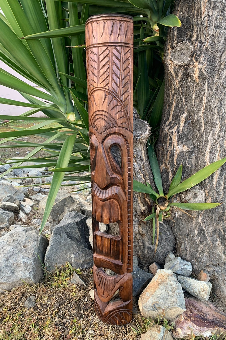 hand-carved wooden totem pole with faces and geometric patterns outdoors beside rocks and plants