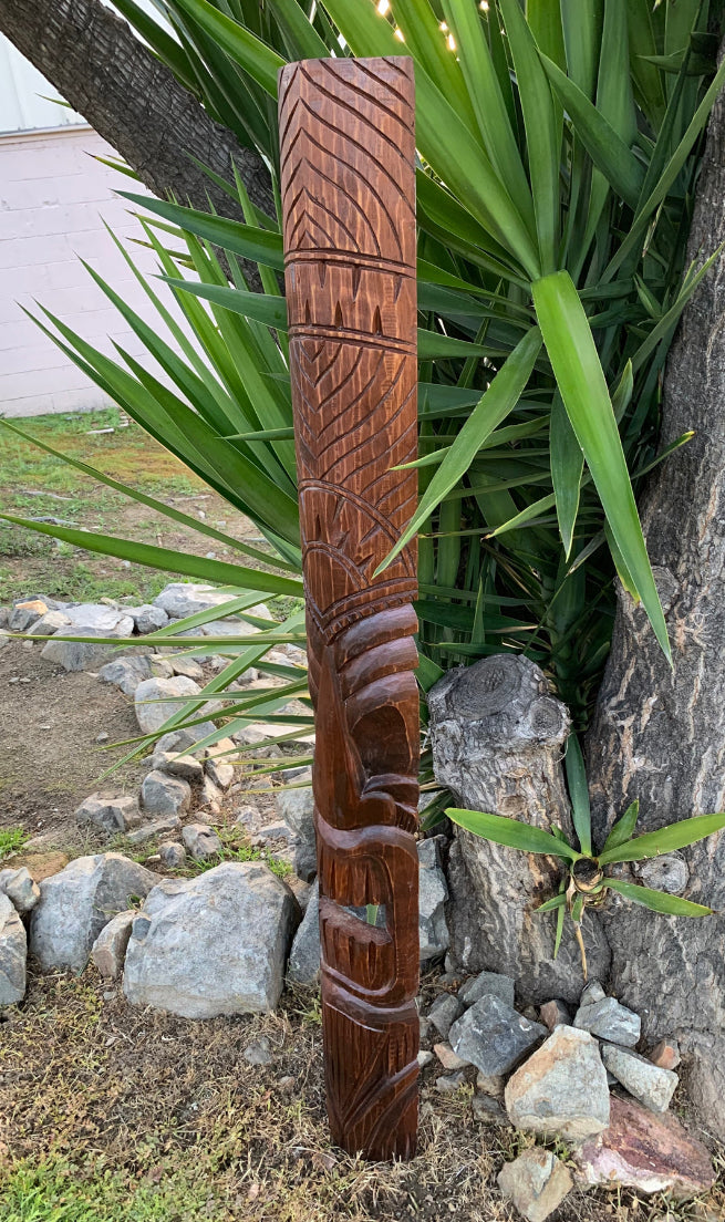 Hand-carved wooden totem pole with geometric patterns in a garden setting.