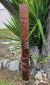 Hand-carved wooden totem pole with geometric patterns in a garden setting.