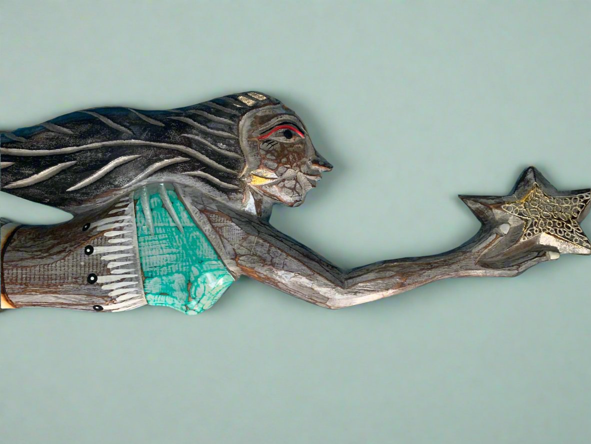 Carved wooden woman reaching for a star with teal clothing and flowing hair.