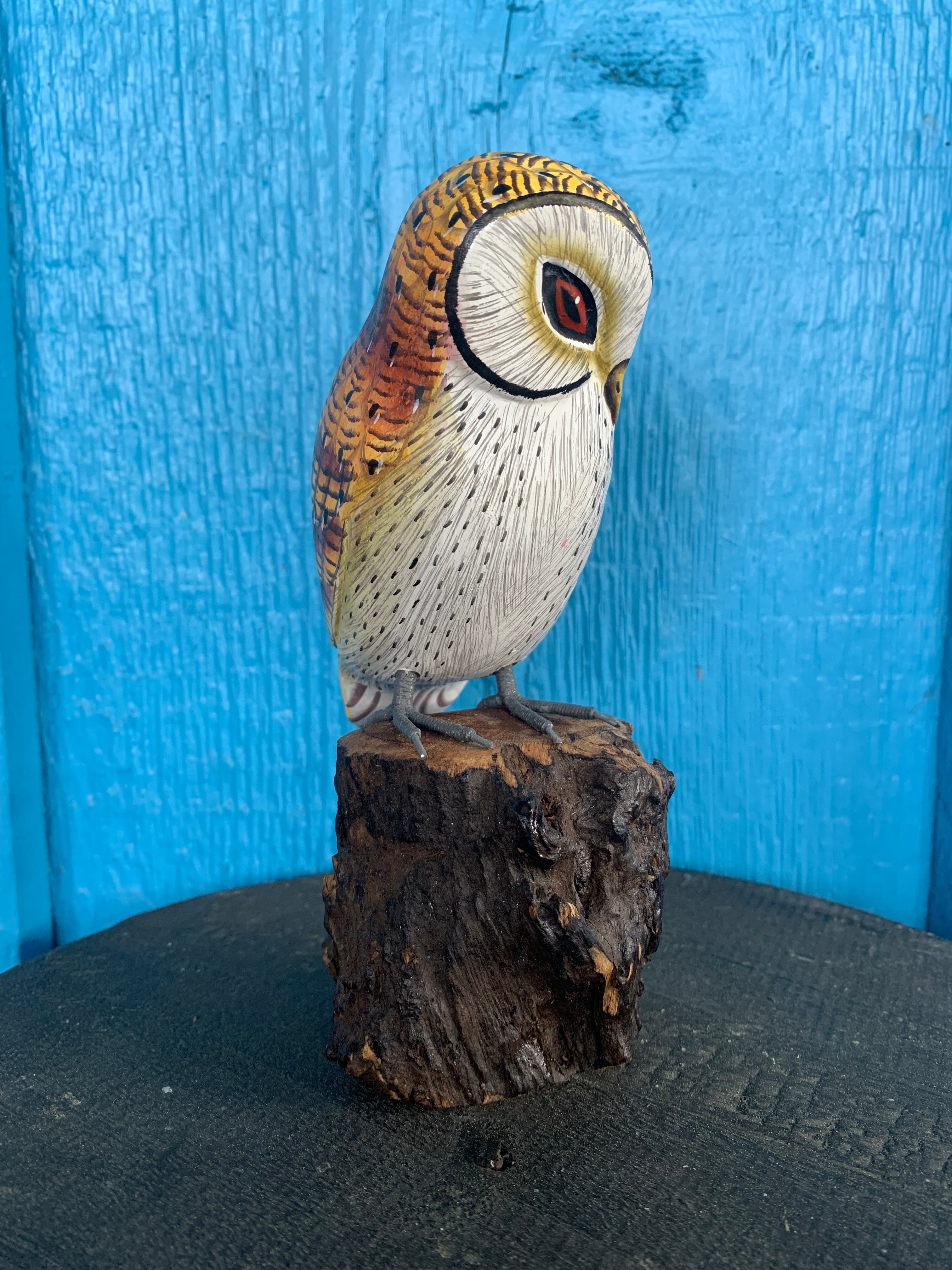 Hand-painted owl figurine perched on a wooden stump against a bright blue background