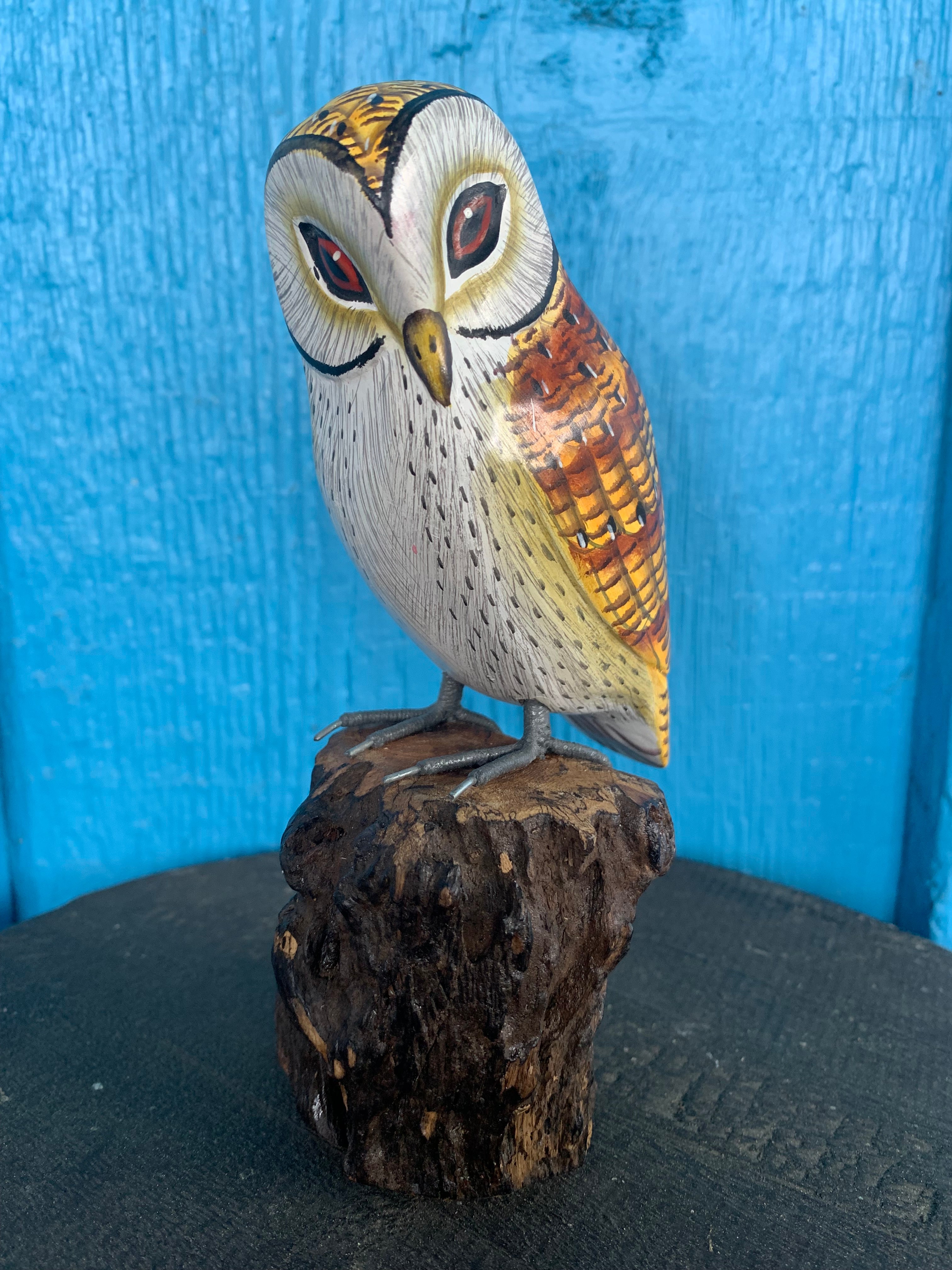 Hand-painted wooden owl figurine perched on a textured brown log against a blue background