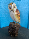 Hand-painted wooden owl figurine perched on a textured brown log against a blue background