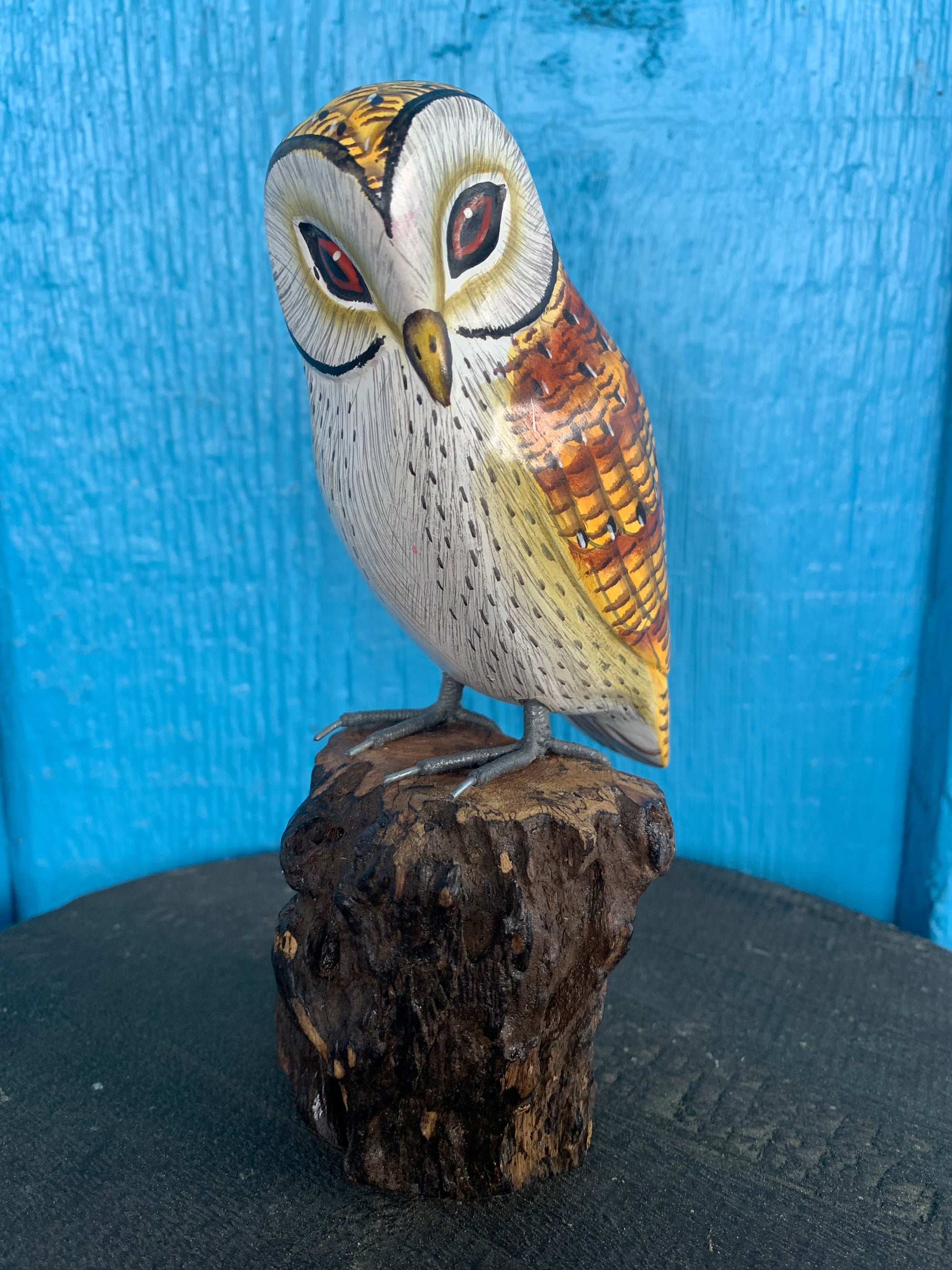 Hand-painted wooden owl figurine perched on a textured brown log against a blue background