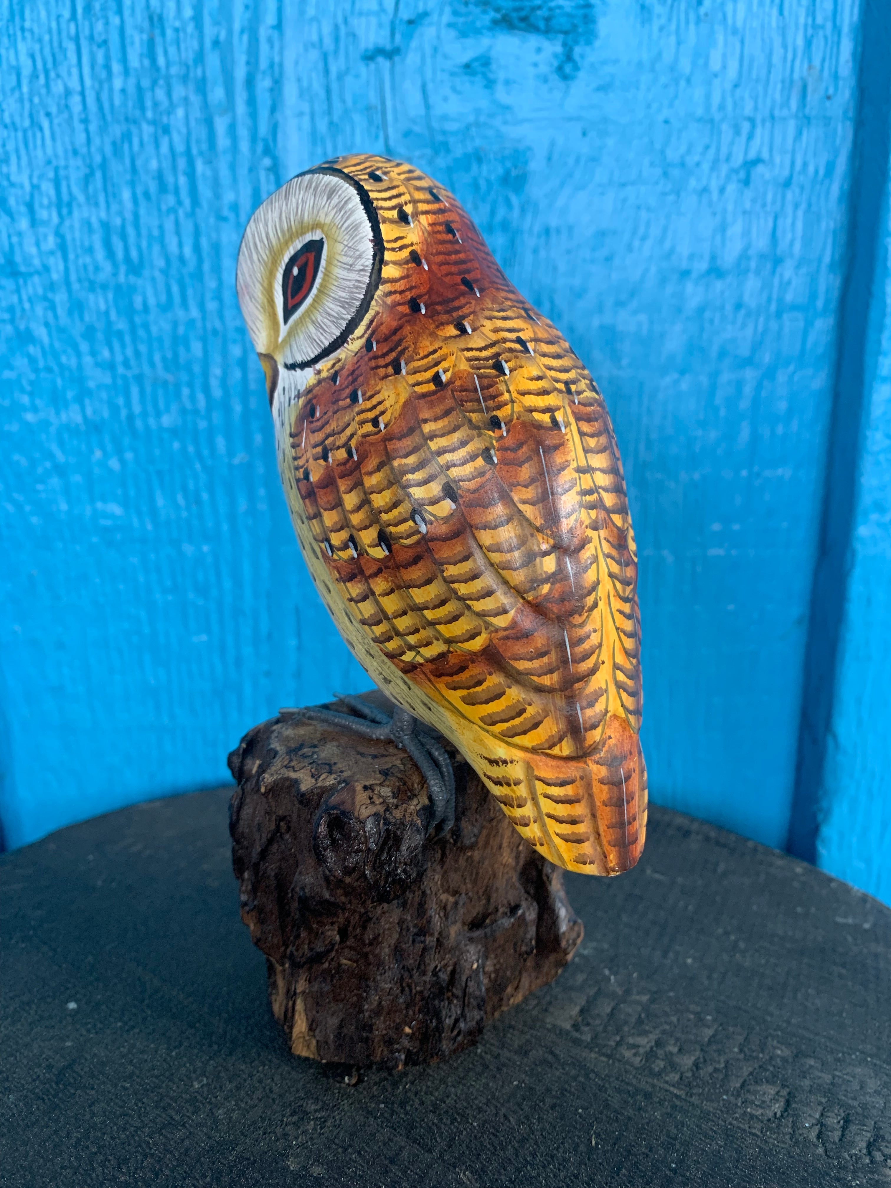 hand-painted-wooden-owl statue perched on a dark wood base with a bright blue background