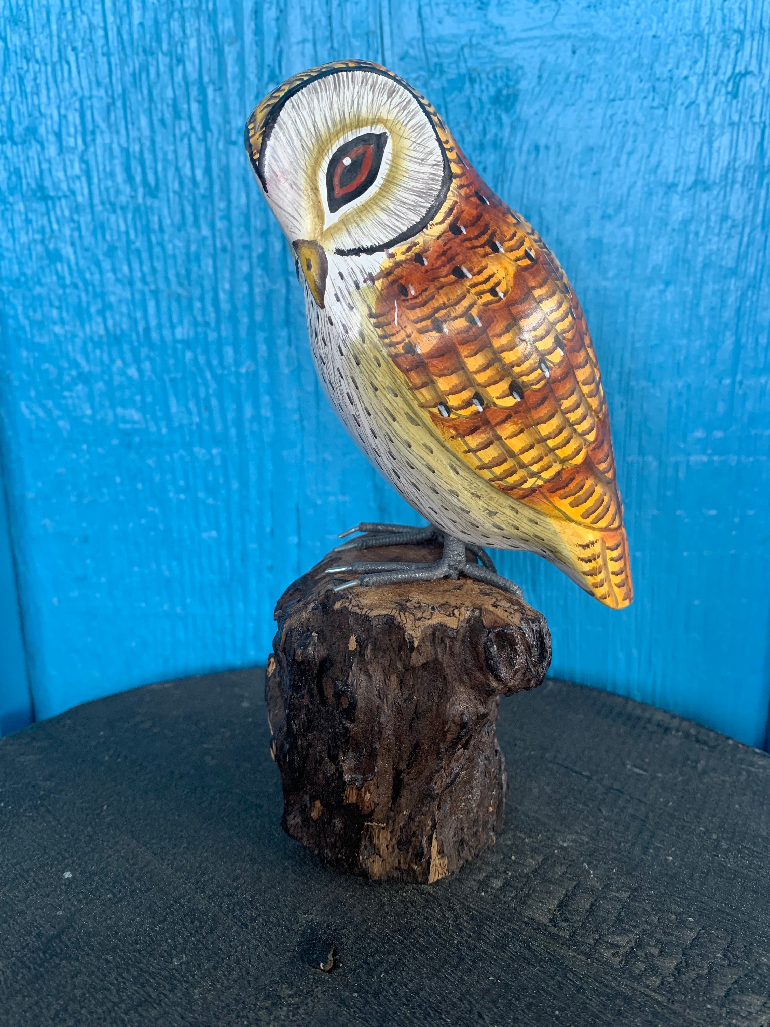 Hand-painted wooden owl statue perched on a log against a blue background.