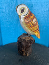 Hand-painted wooden owl statue perched on a log against a blue background.