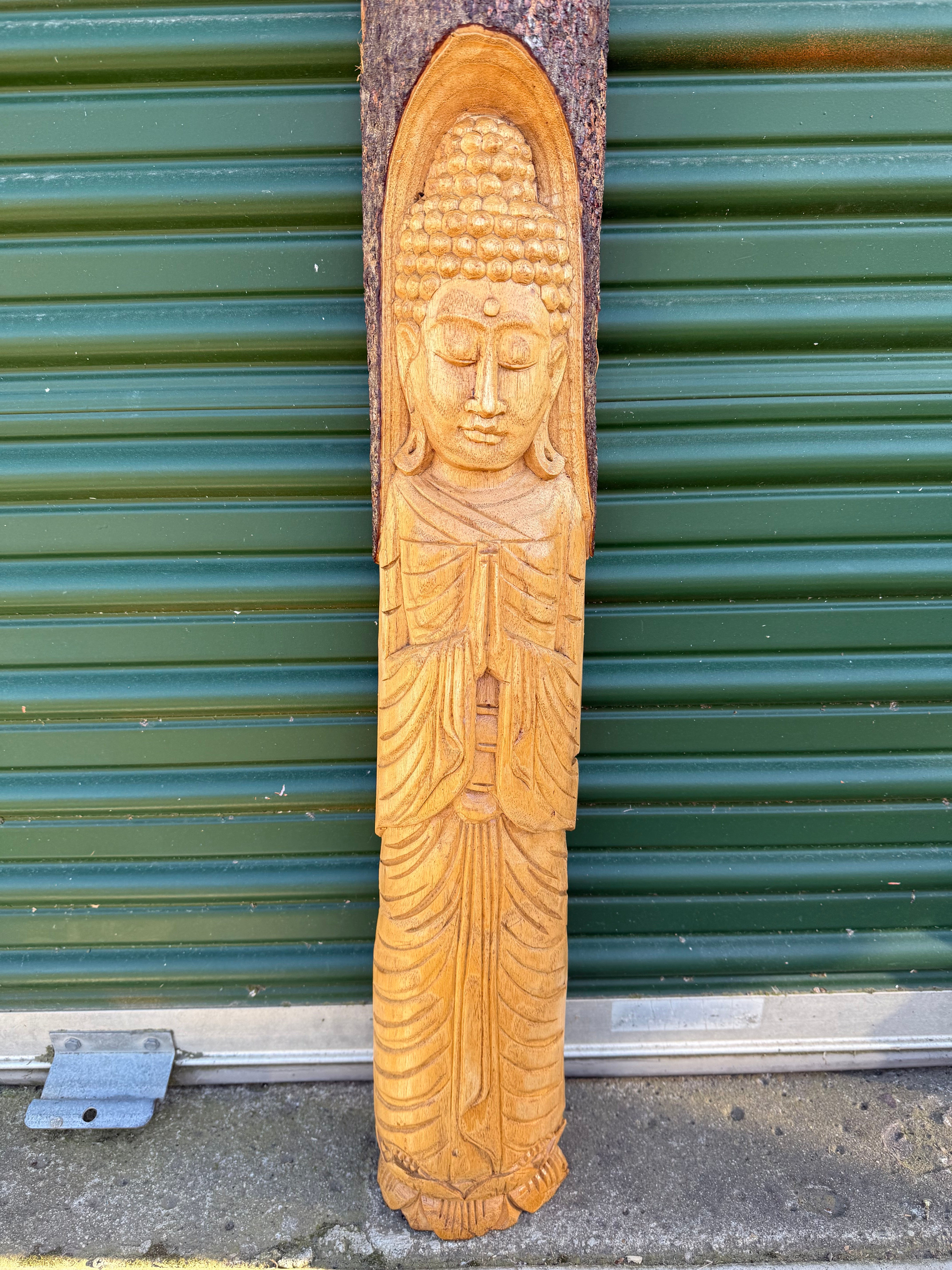 Hand-carved wooden Buddha statue in prayer position against a green corrugated metal background