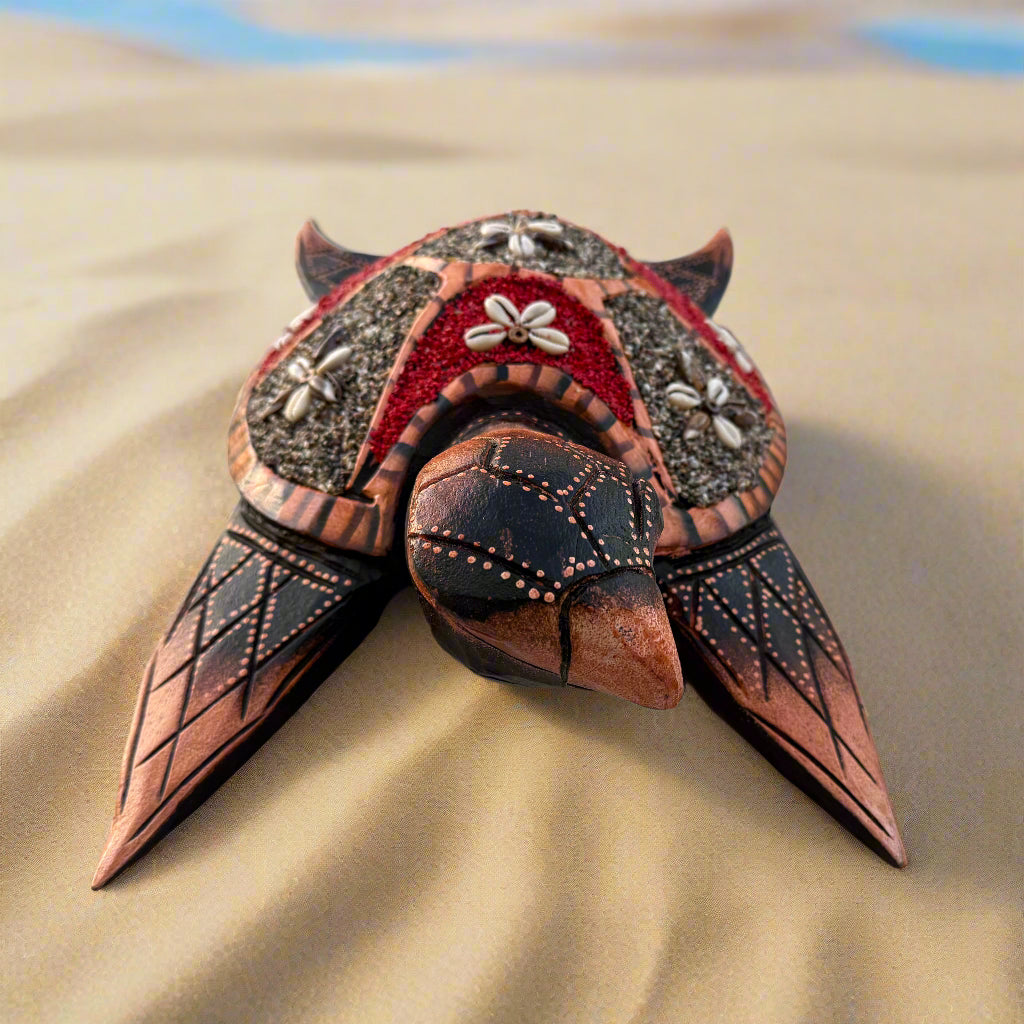 Decorative wooden turtle with ornate shell patterns and floral embellishments on a sandy beach.
