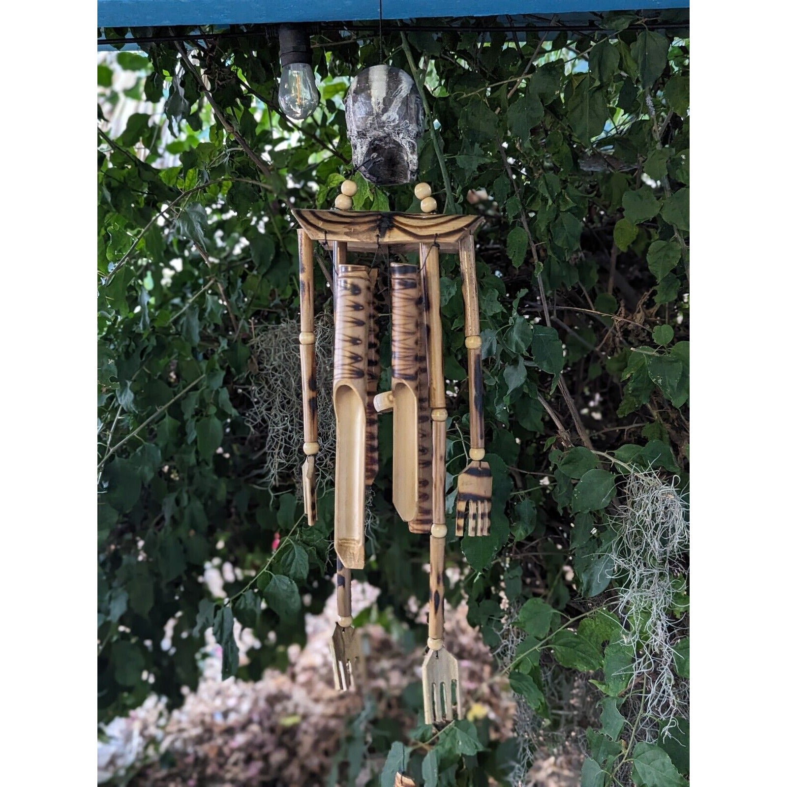 Handcrafted wooden bamboo wind chimes hanging among greenery in a garden