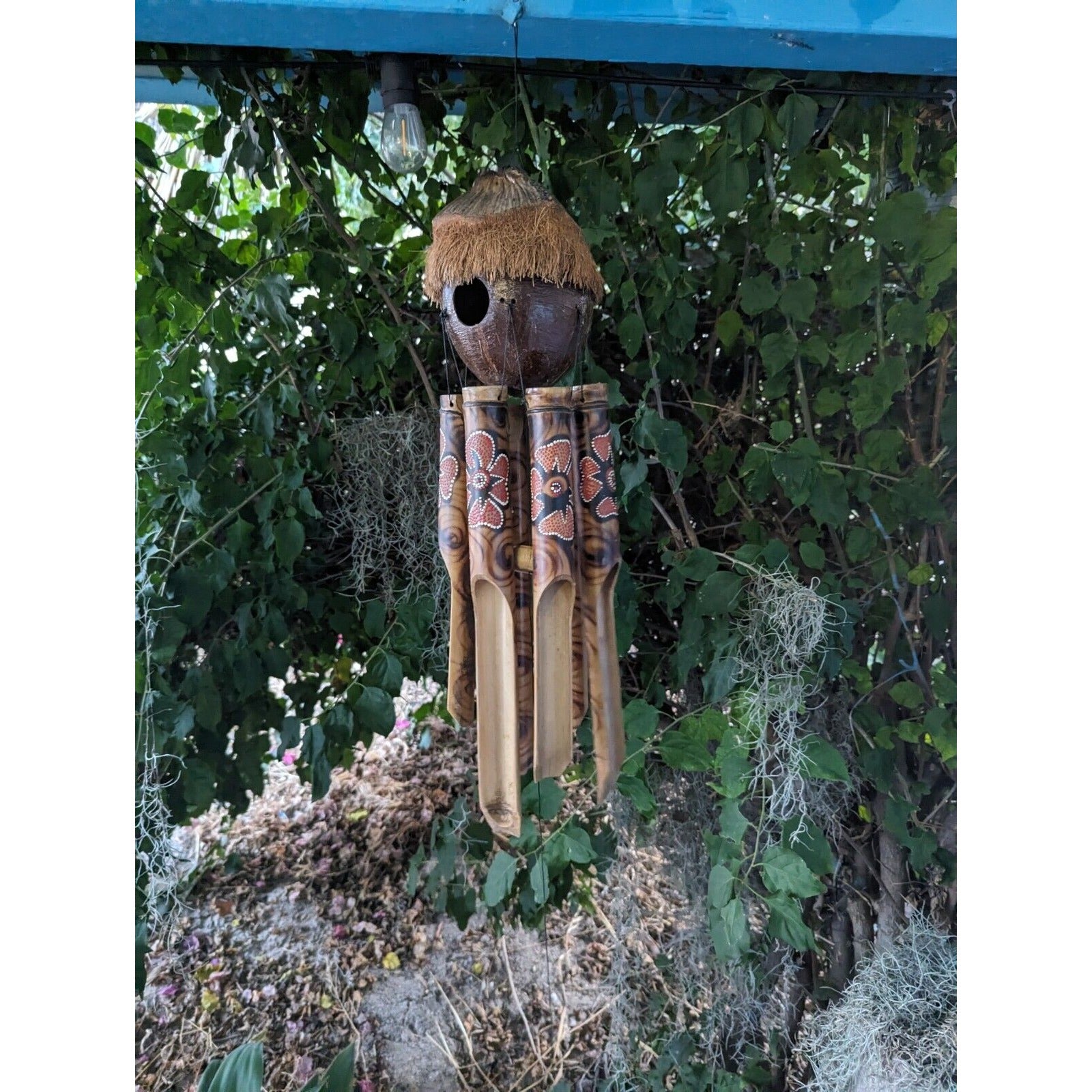 handmade bamboo wind chime with coconut-shell birdhouse and thatched roof hanging in a garden