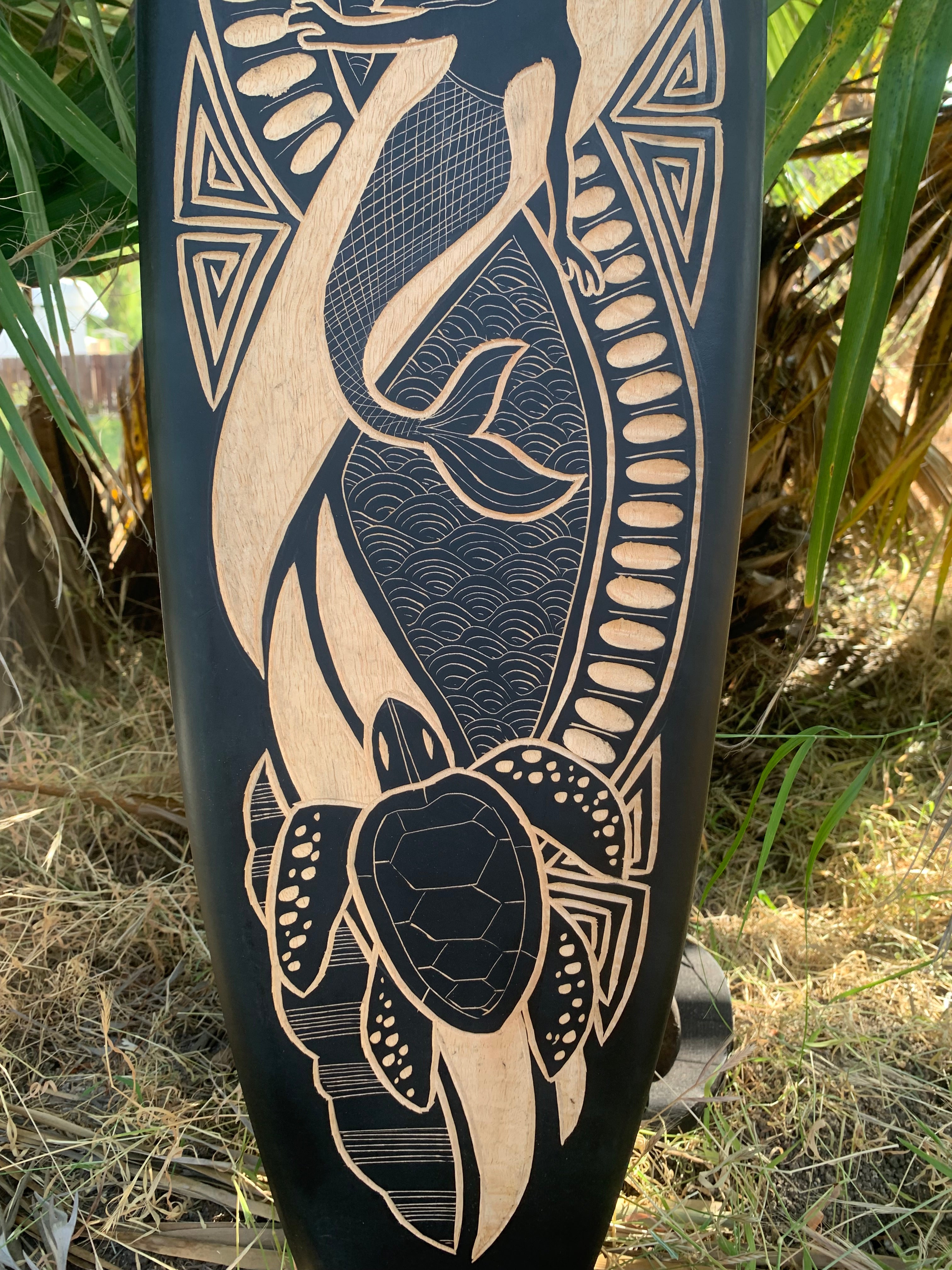Intricate wood-carved sea turtle on dark panel with geometric shapes and wave textures