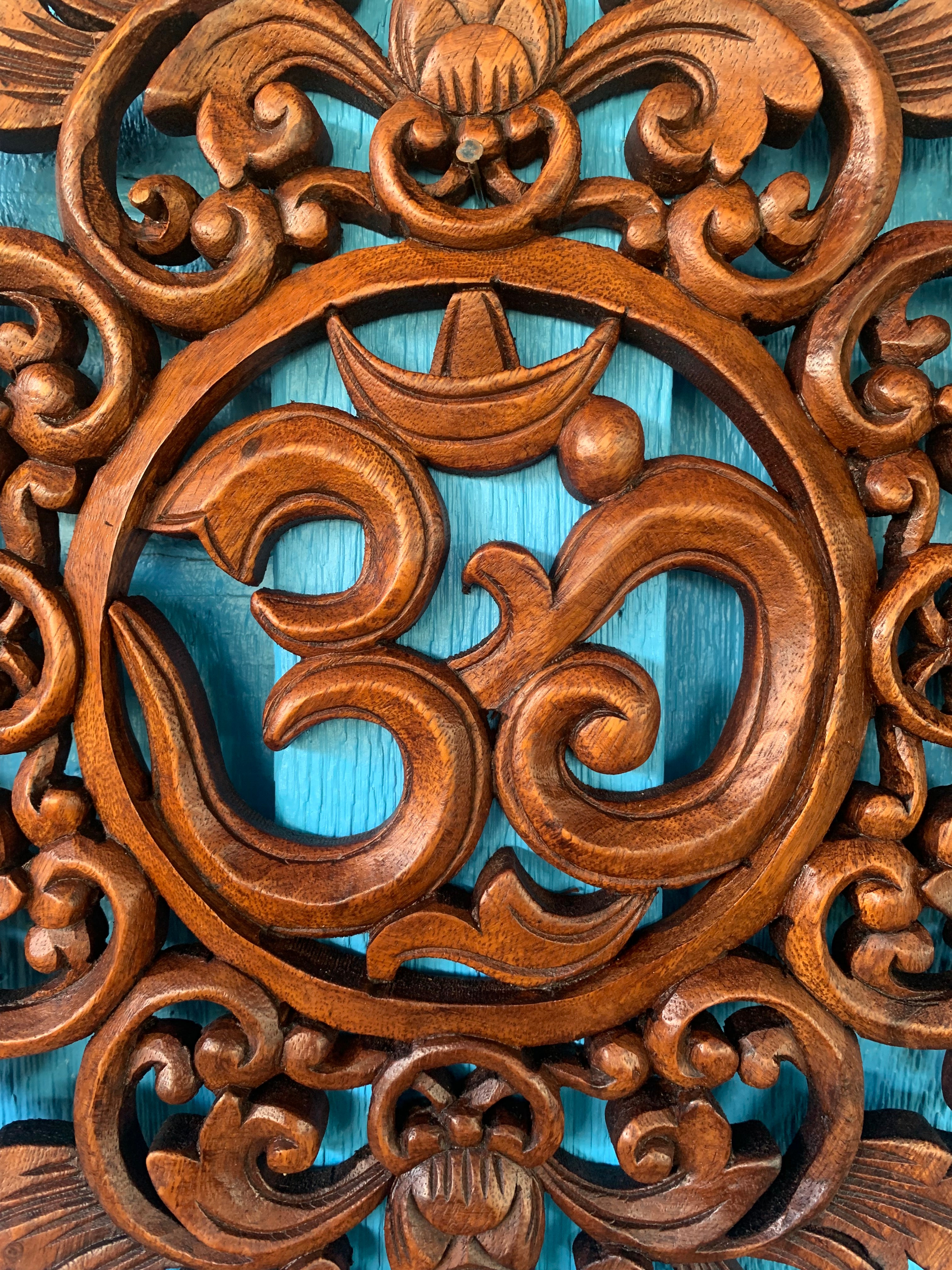 Intricate wooden Om symbol carving with ornate scrollwork on turquoise background.