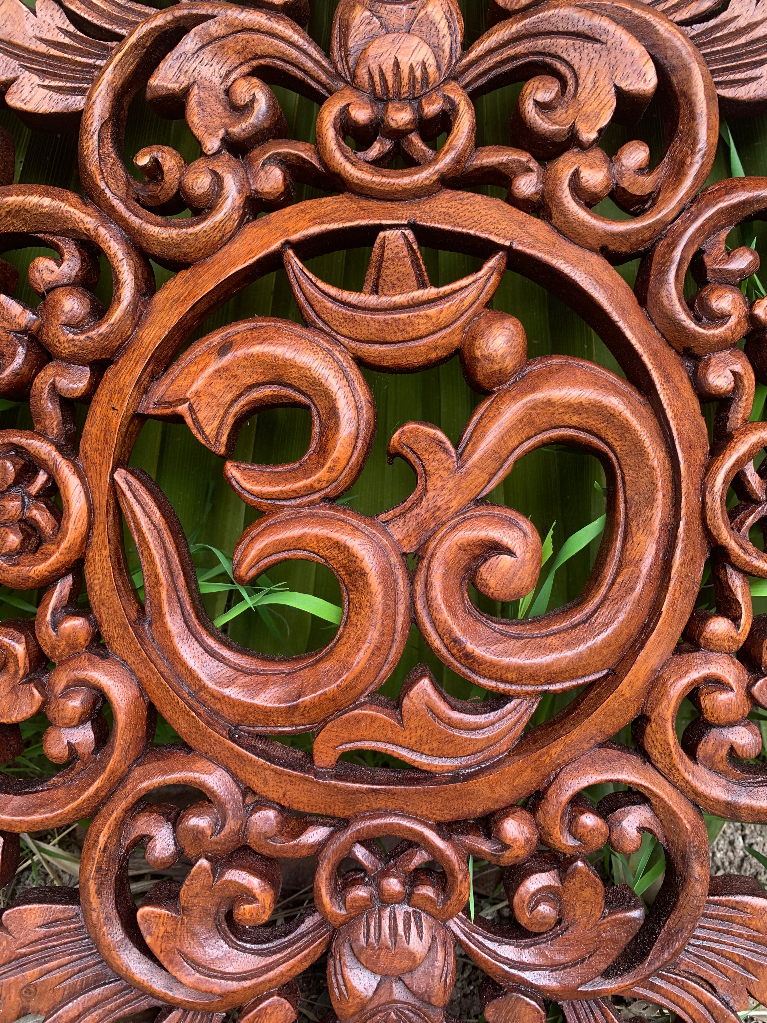 Intricate wooden circular carving featuring the Om symbol with ornate scrollwork and greenery in the background