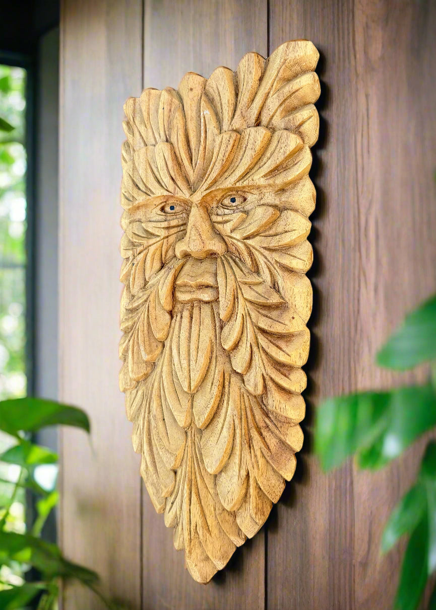 Intricately carved wooden face mask with leaf-like pattern mounted on a wooden wall