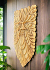 Intricately carved wooden face mask with leaf-like pattern mounted on a wooden wall