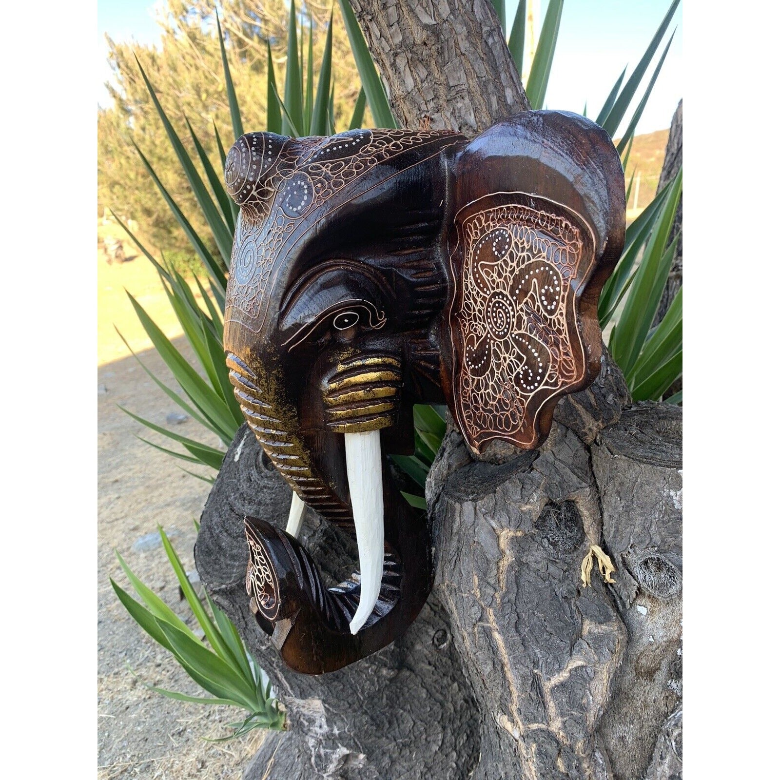 Carved wooden elephant head sculpture with decorative patterns mounted on a tree