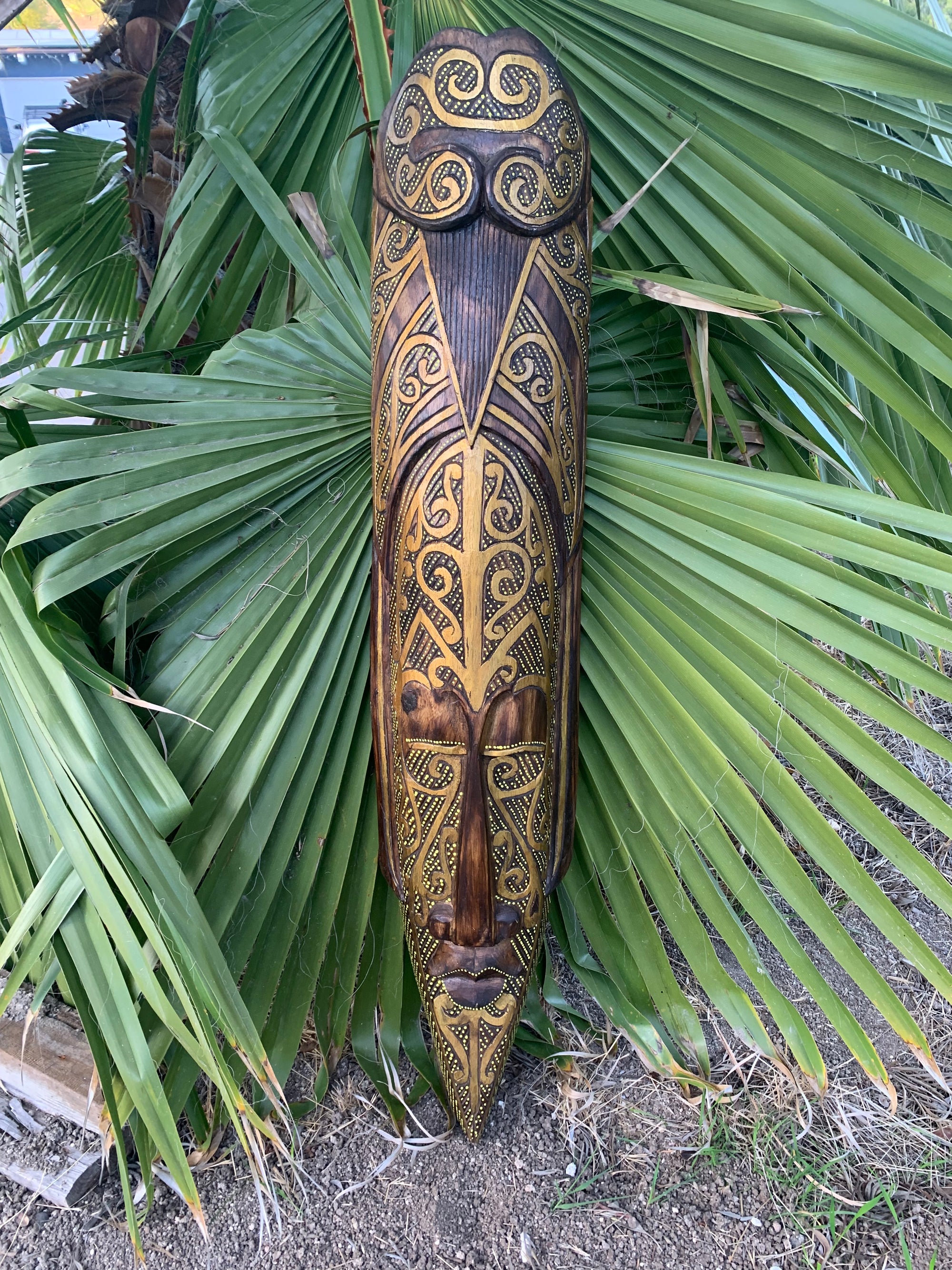 Intricately carved wooden mask with gold detailing among palm fronds
