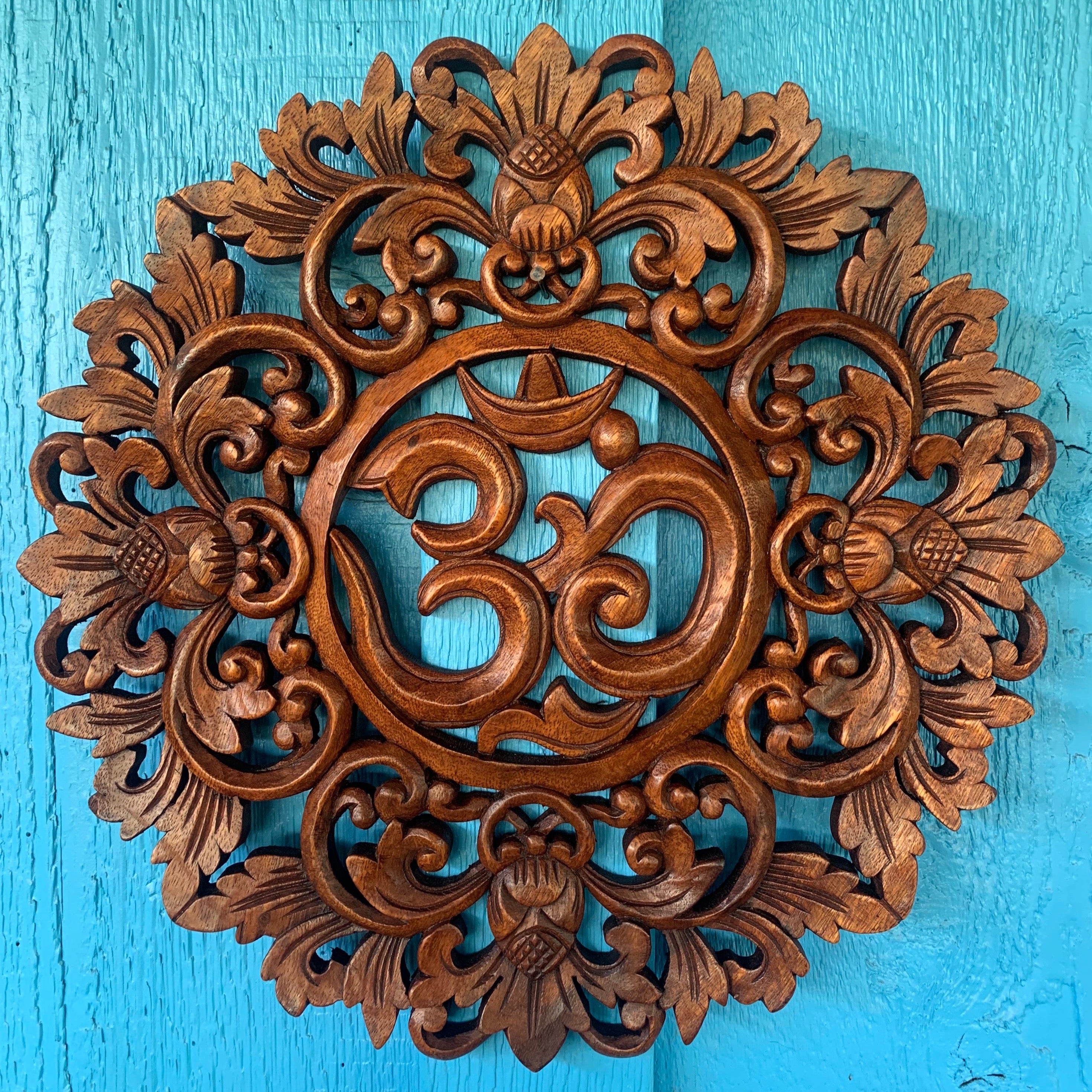 Intricately carved wooden Om symbol mandala wall hanging with floral motifs on a turquoise background