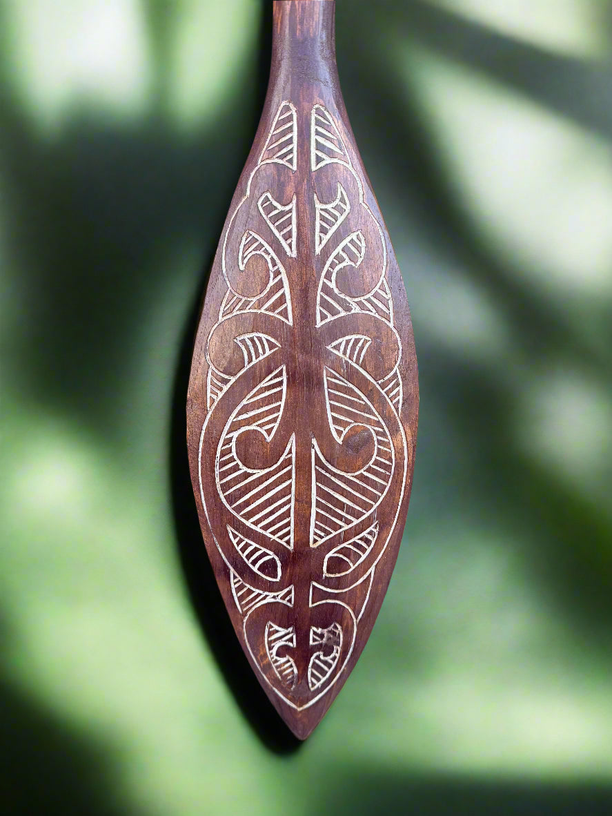 intricately carved wooden paddle with white tribal patterns