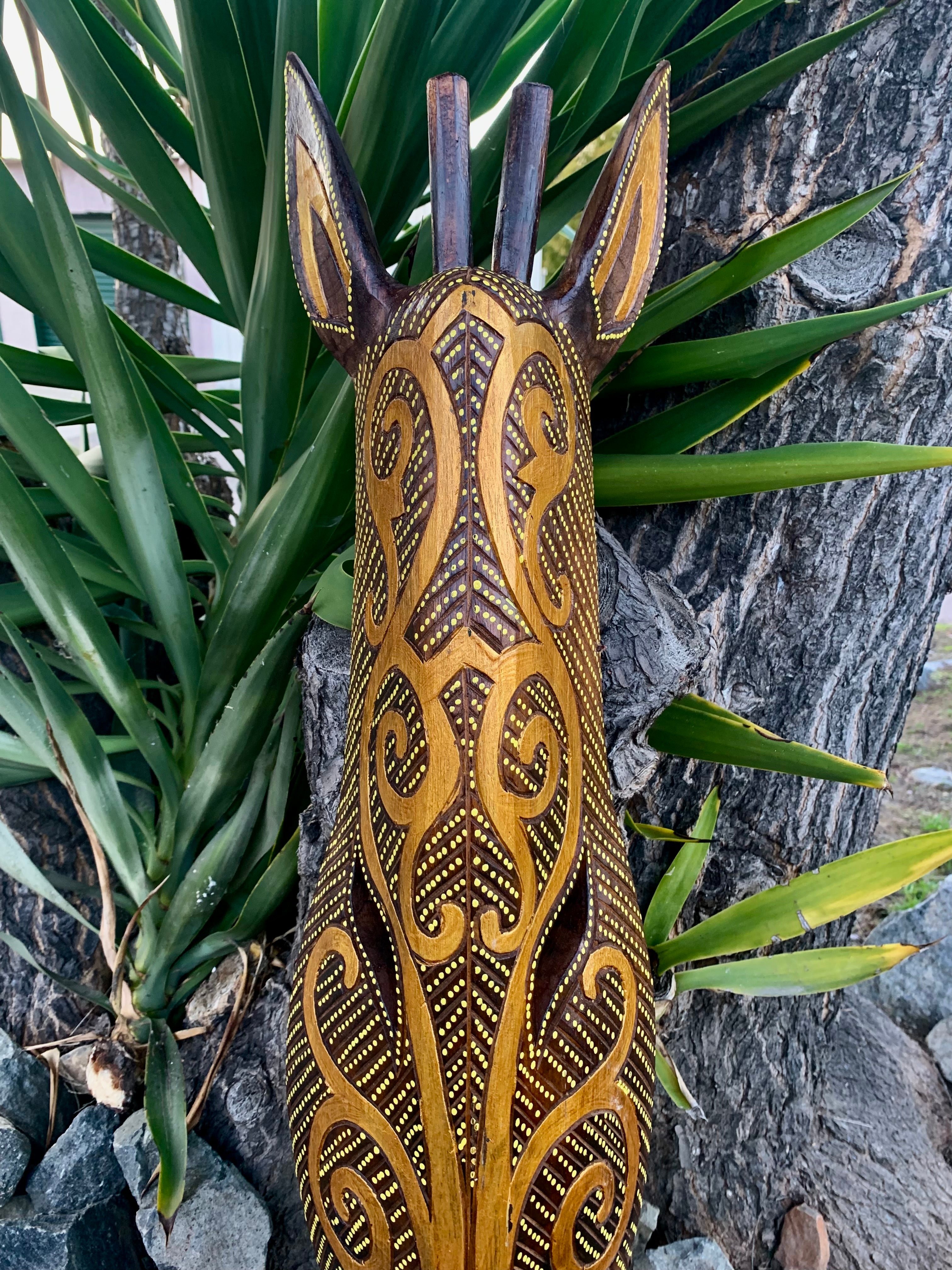 Intricately carved wooden sculpture with yellow dotted patterns leaning against a tree