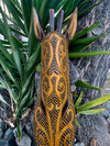 Intricately carved wooden sculpture with yellow dotted patterns leaning against a tree