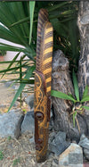 intricately carved wooden staff with dot patterns and scrolling designs leaning beside a tree