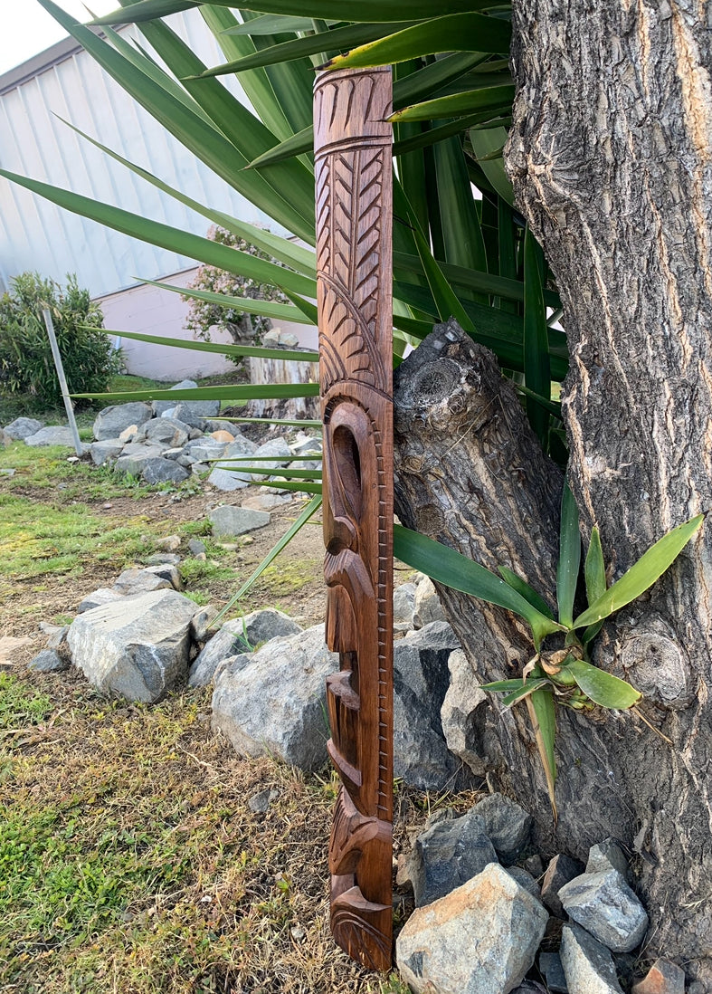 Intricately carved wooden staff with geometric patterns leaning against a tree outdoors