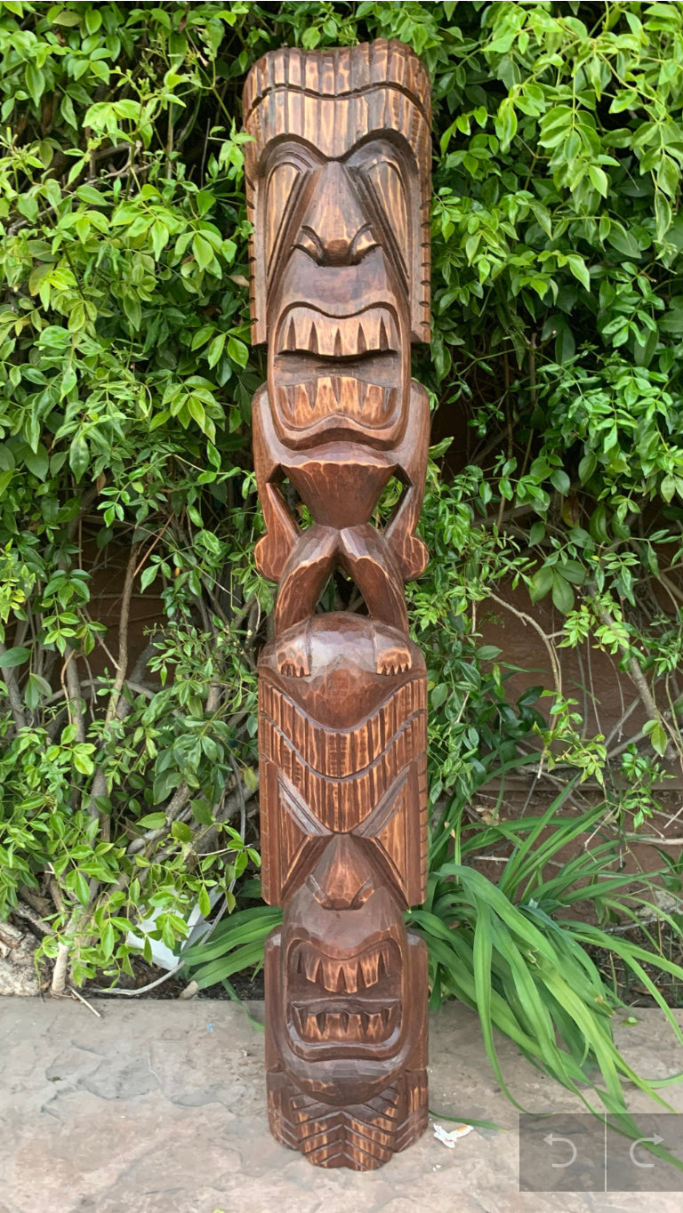 Carved wooden totem pole with multiple fierce faces in lush green foliage