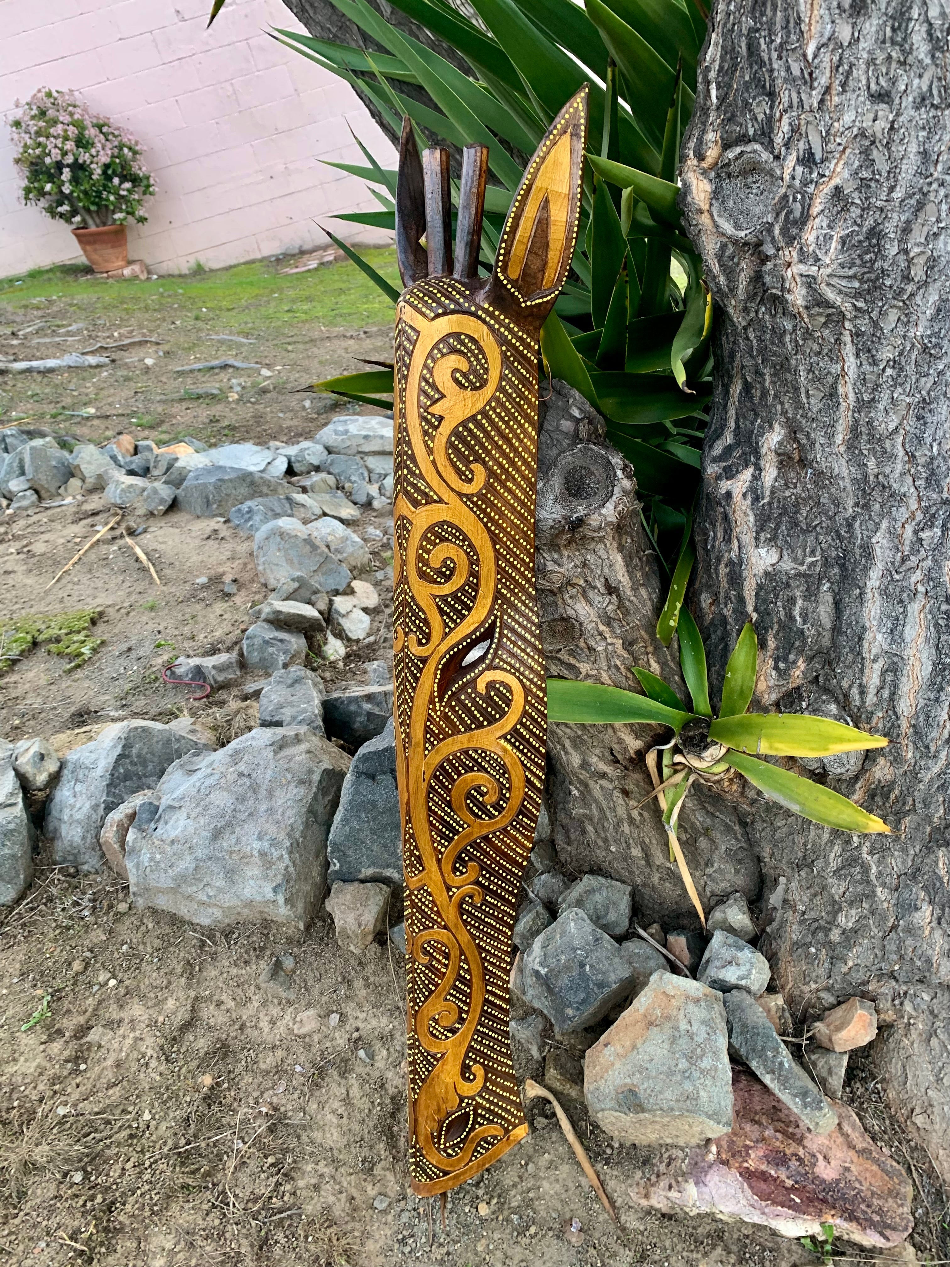 intricately carved wooden totem staff with gold swirl patterns and dotted detailing leaning against a tree