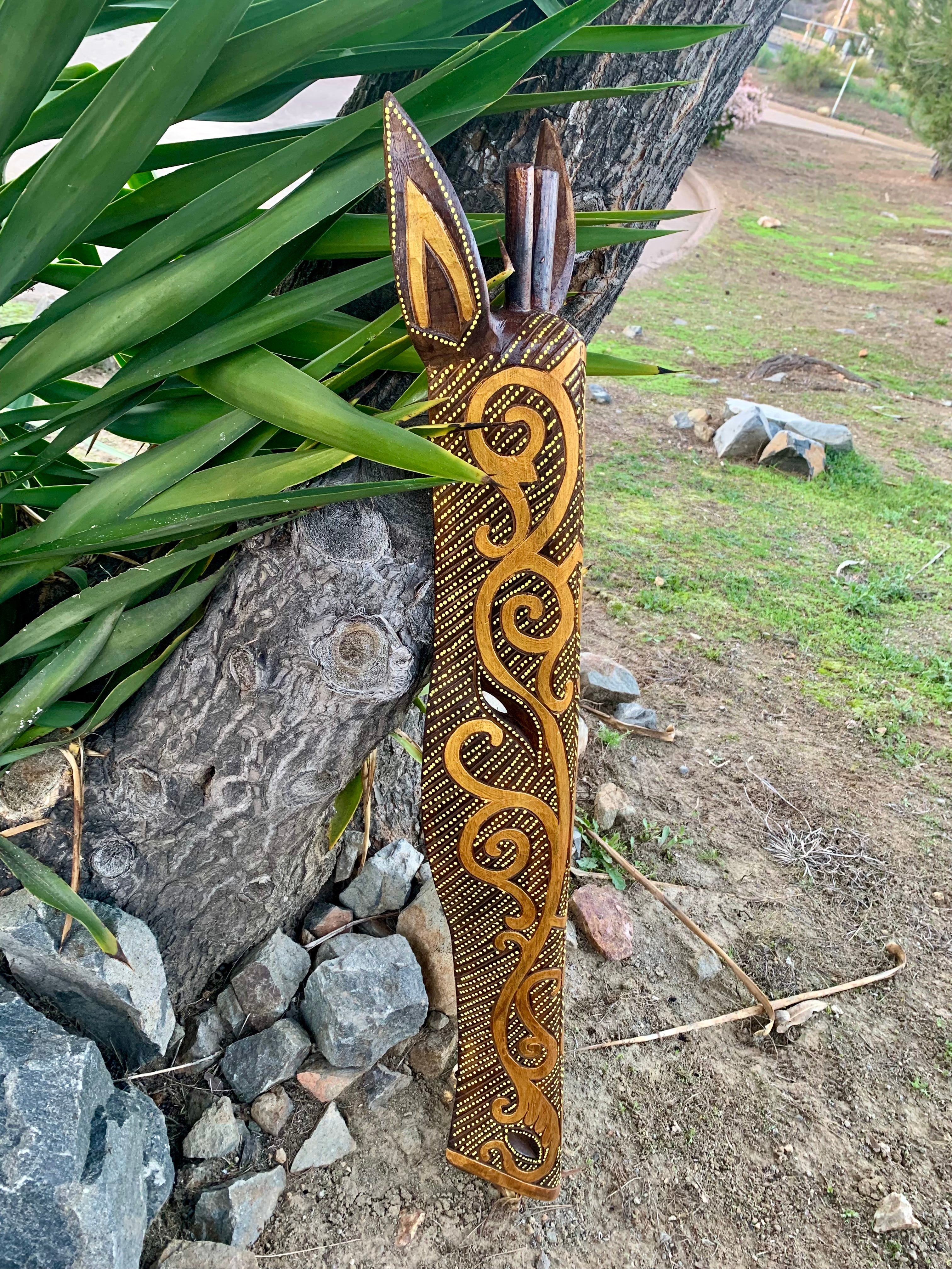 Wooden carved totem staff with golden spiral patterns leaning against a tree