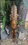 Intricately carved wooden tribal mask with geometric patterns leaning against a tree.