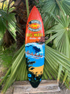 Colorful Kona Big Wave surfboard with palm-tree sunset and ocean wave design