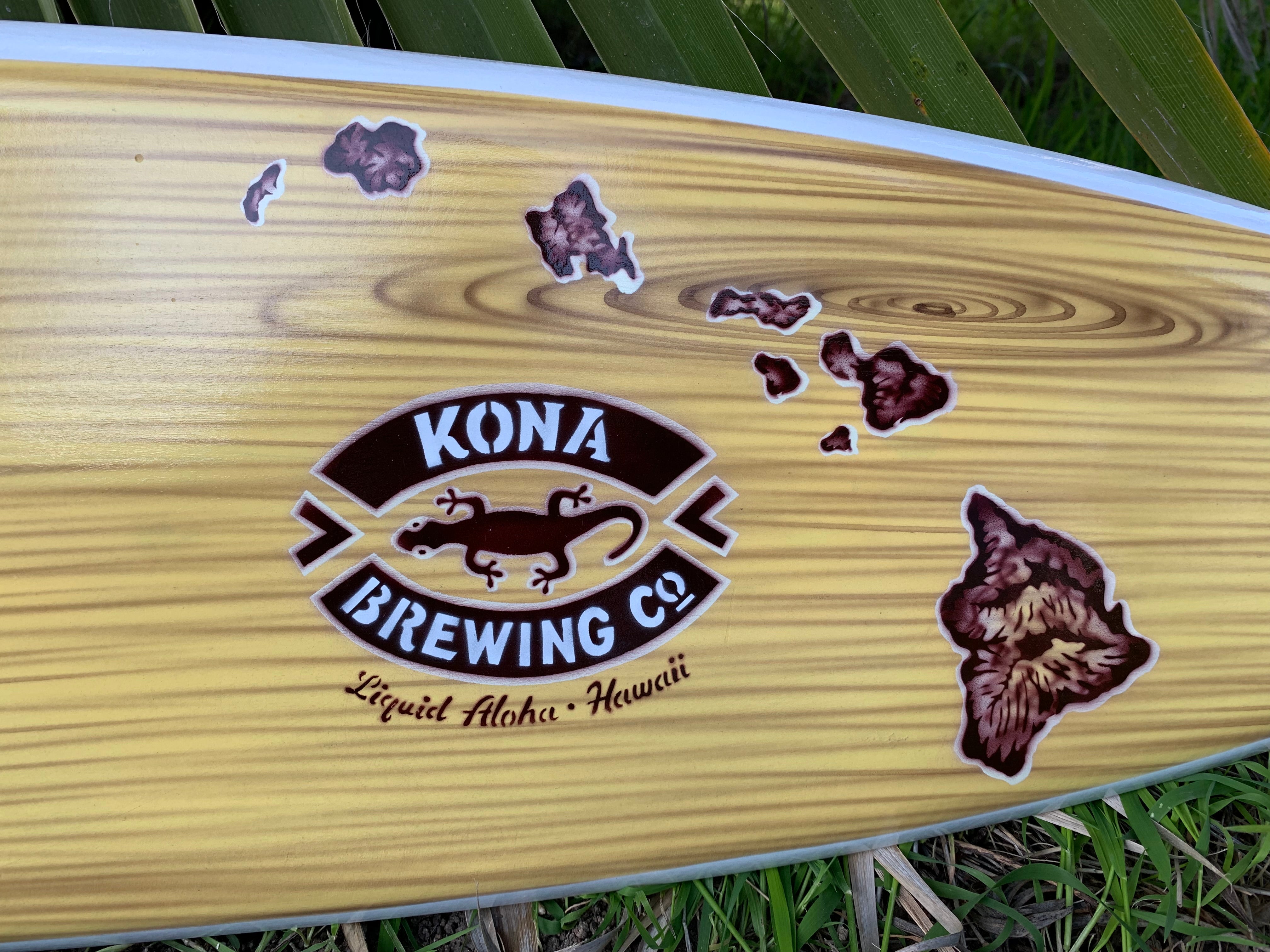 Kona Brewing Co logo on wooden surfboard with Hawaii island stickers