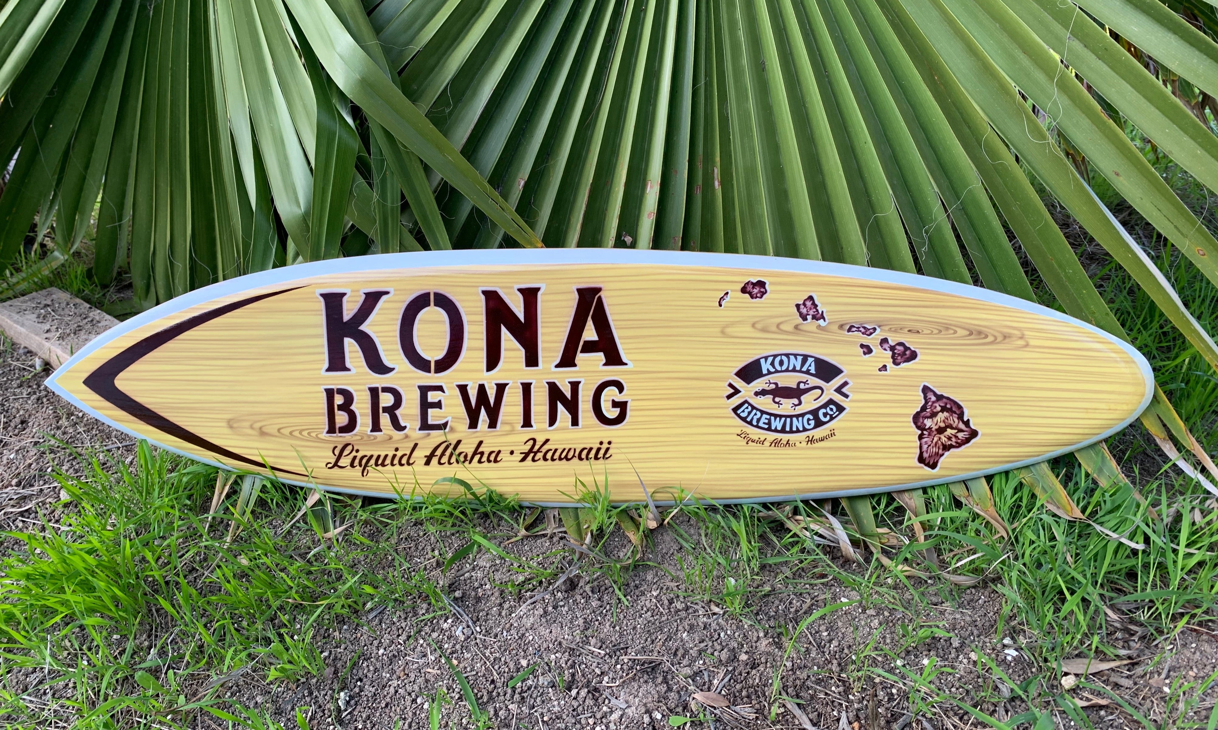 Kona Brewing surfboard sign with logo against tropical leaves