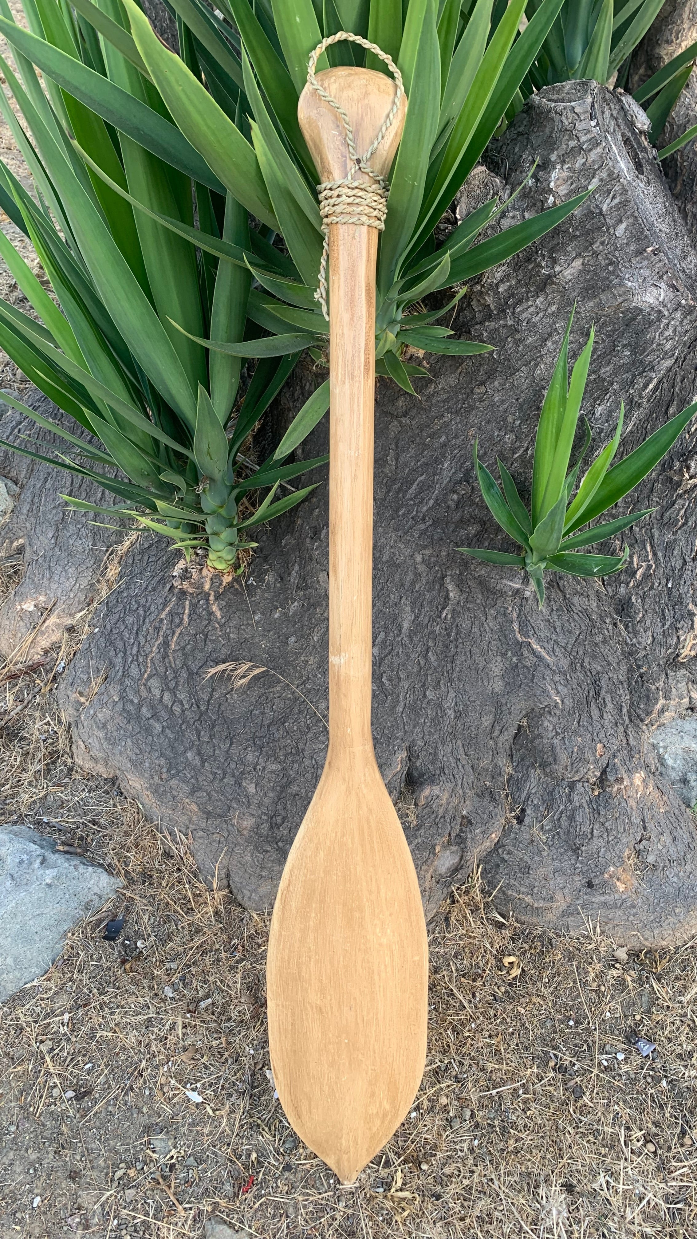 wooden paddle with rope-wrapped handle resting beside green plants outdoors