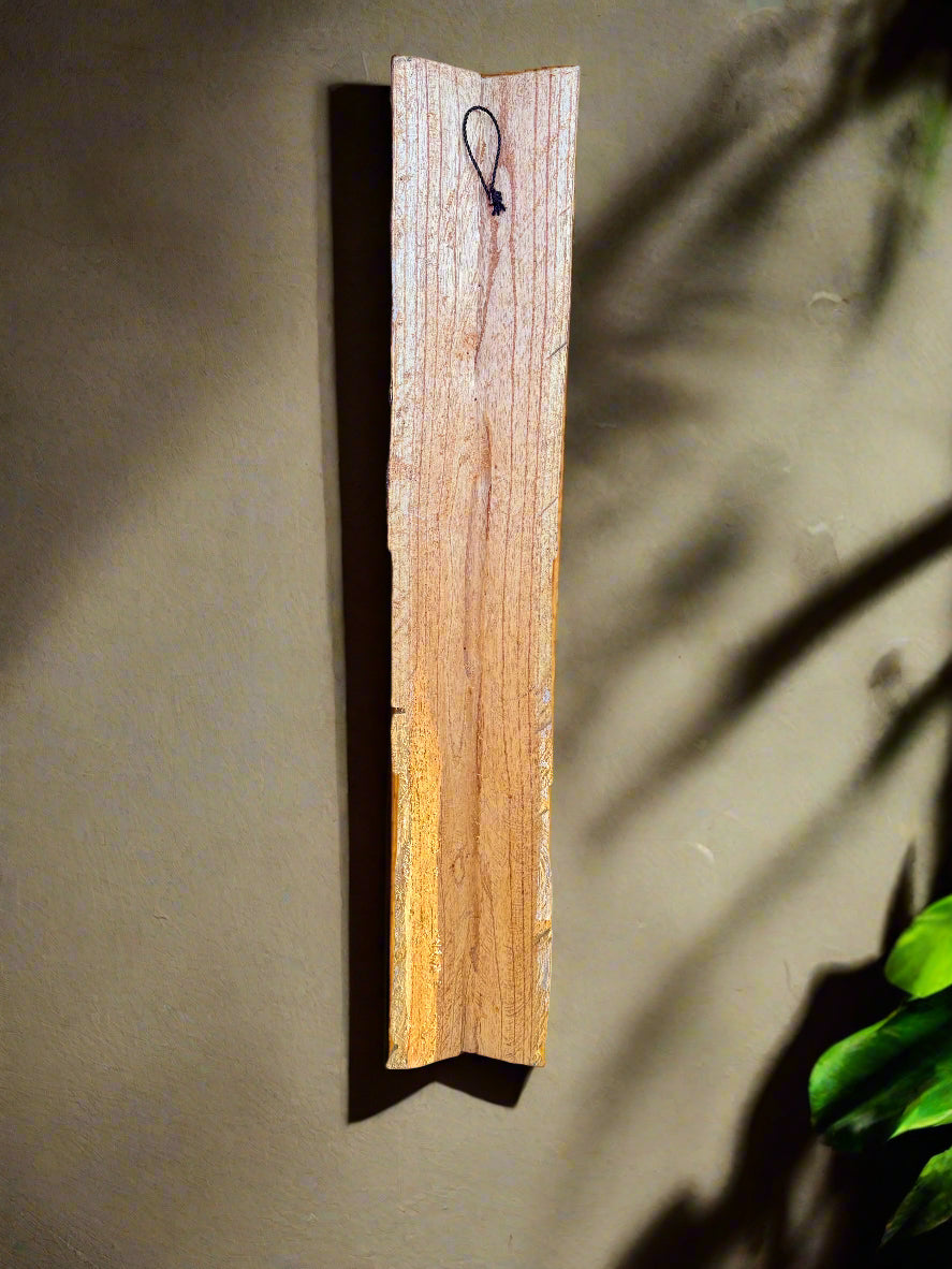 Tall wooden plank mounted on a beige wall with a small black loop at the top.