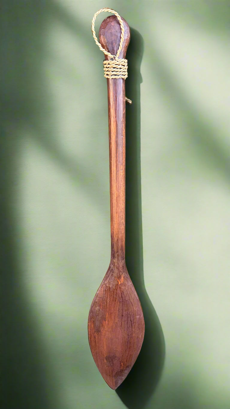 long wooden spoon with looped rope hanging on green background