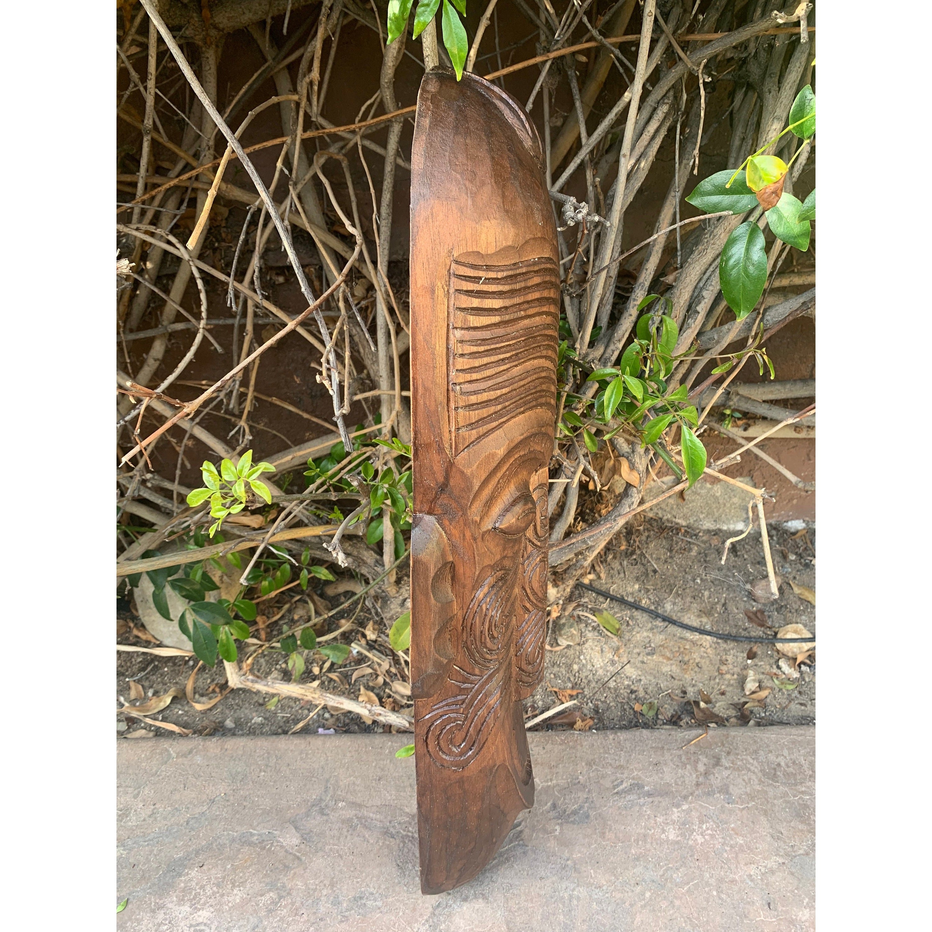 Carved wooden staff with spiral and ridged patterns leaning against garden vines