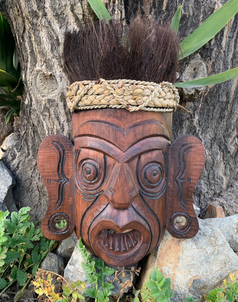 Wooden Maori tiki mask with braided headband and spiky hair.