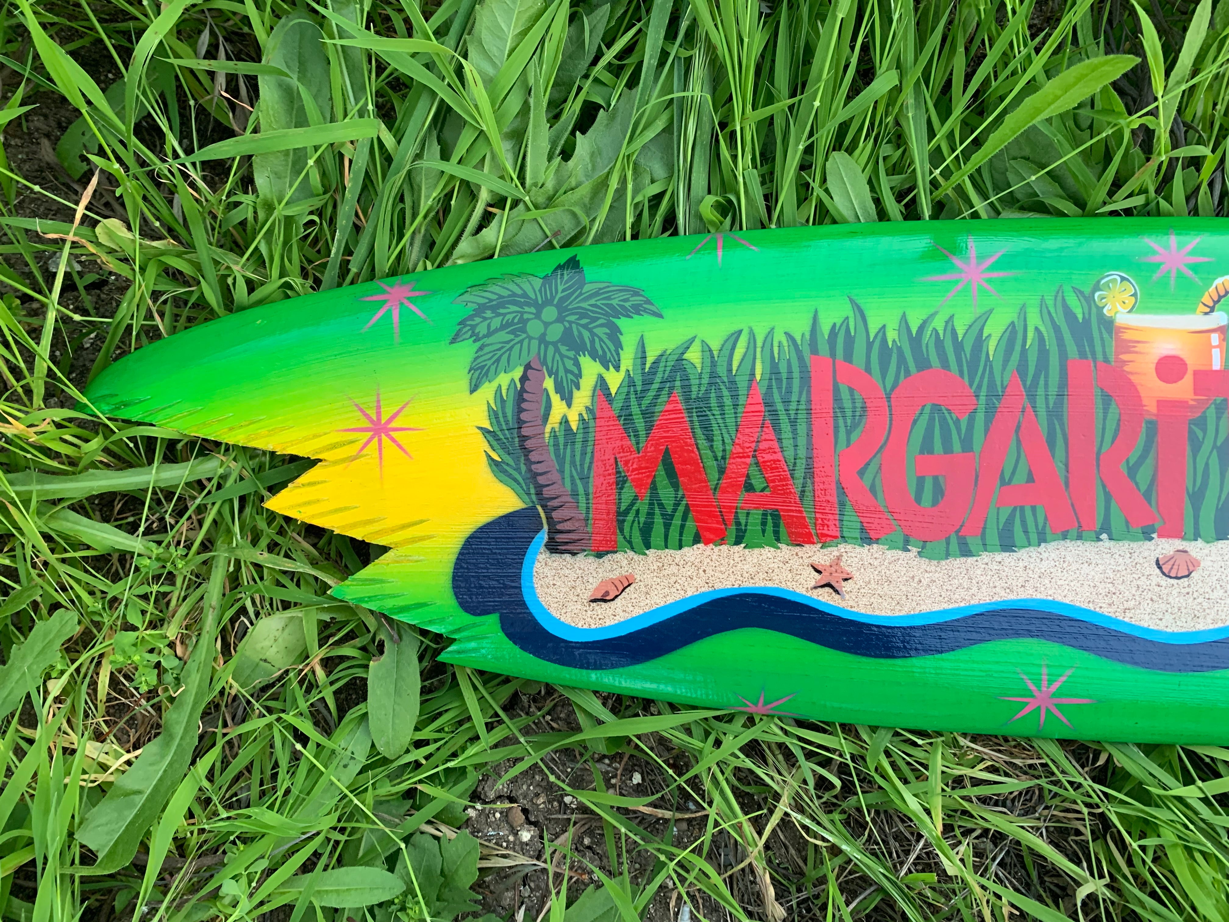 Bright green margarita-themed tropical surfboard on grass with palm trees and waves.