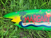 Bright green margarita-themed tropical surfboard on grass with palm trees and waves.