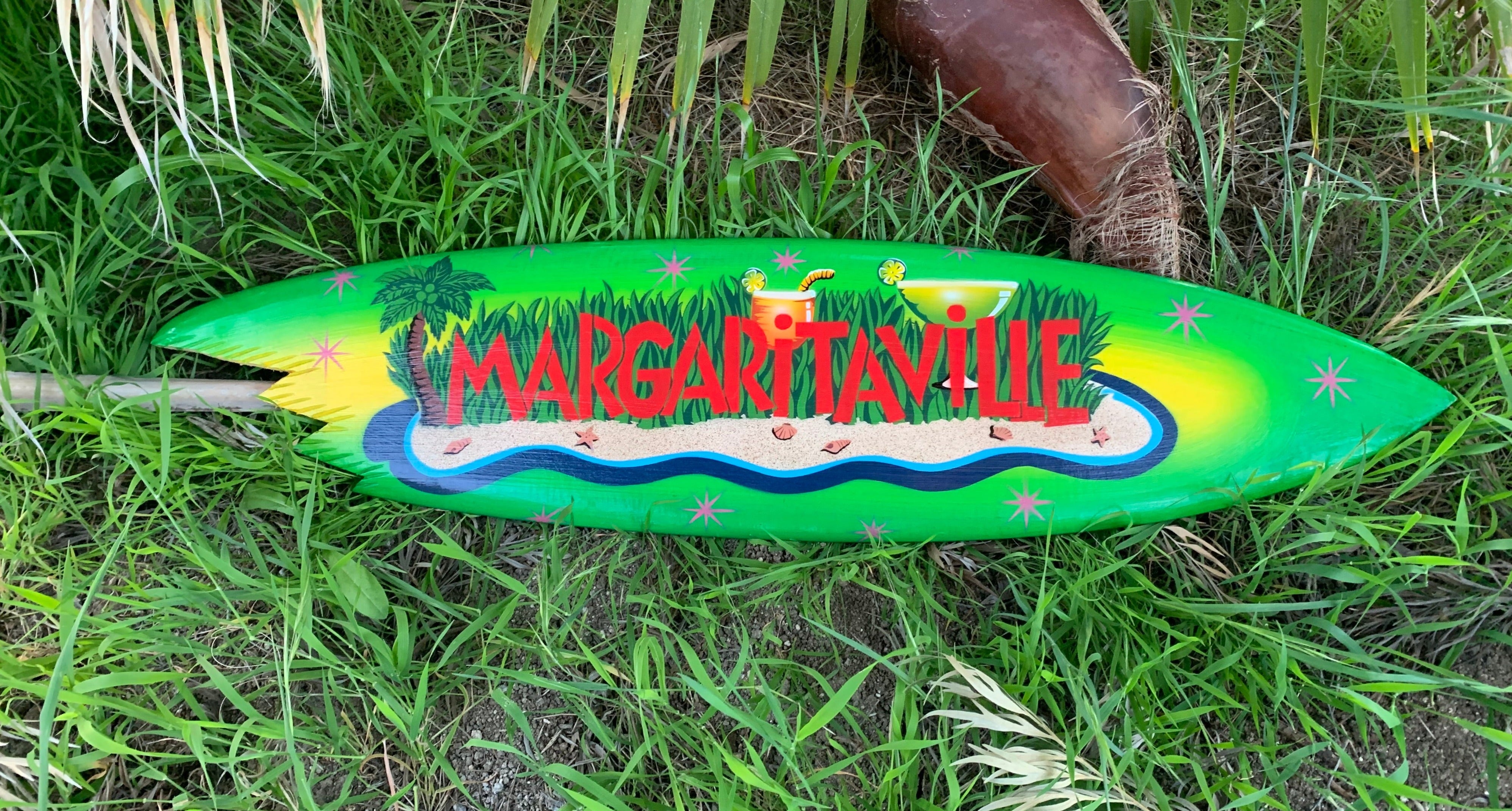 Bright green surfboard with Margarita Ville tropical beach scene on grass