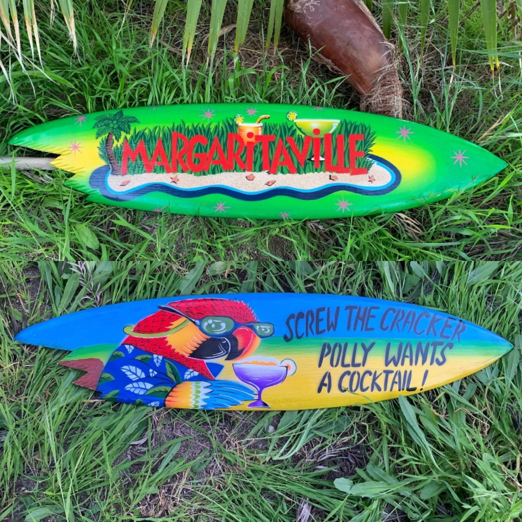 two colorful surfboards with Margaritaville and cocktail graphics resting in grass