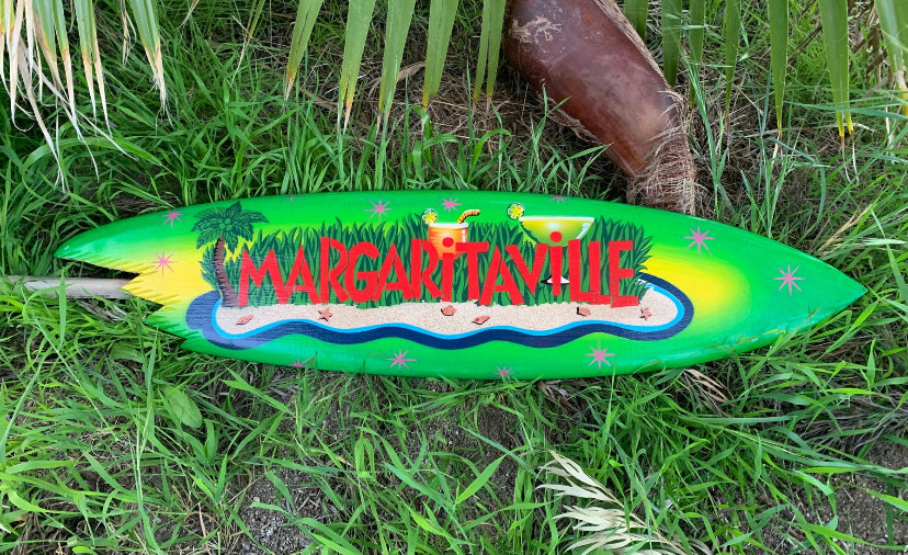 Bright green Margaritaville surfboard with a tropical island scene laid on grass