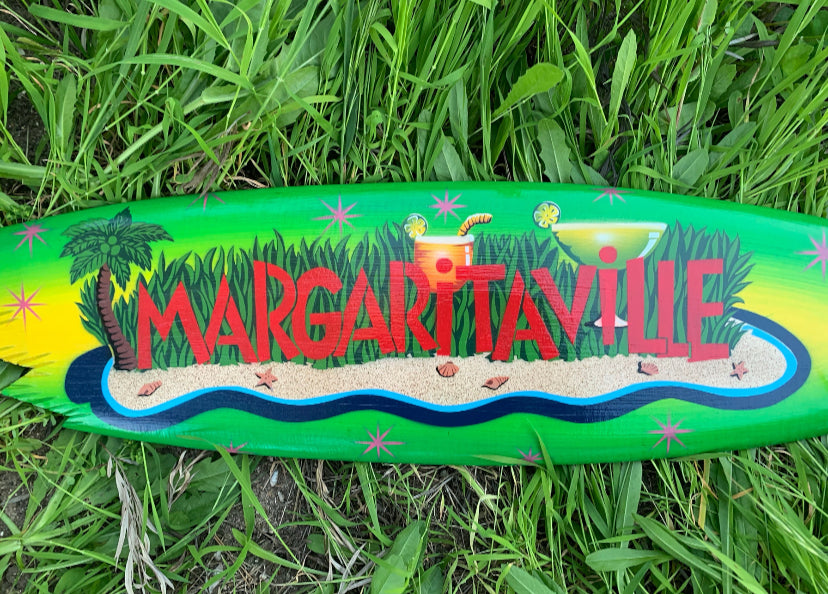 Colorful Margaritaville surfboard with tropical beach scene on green grass