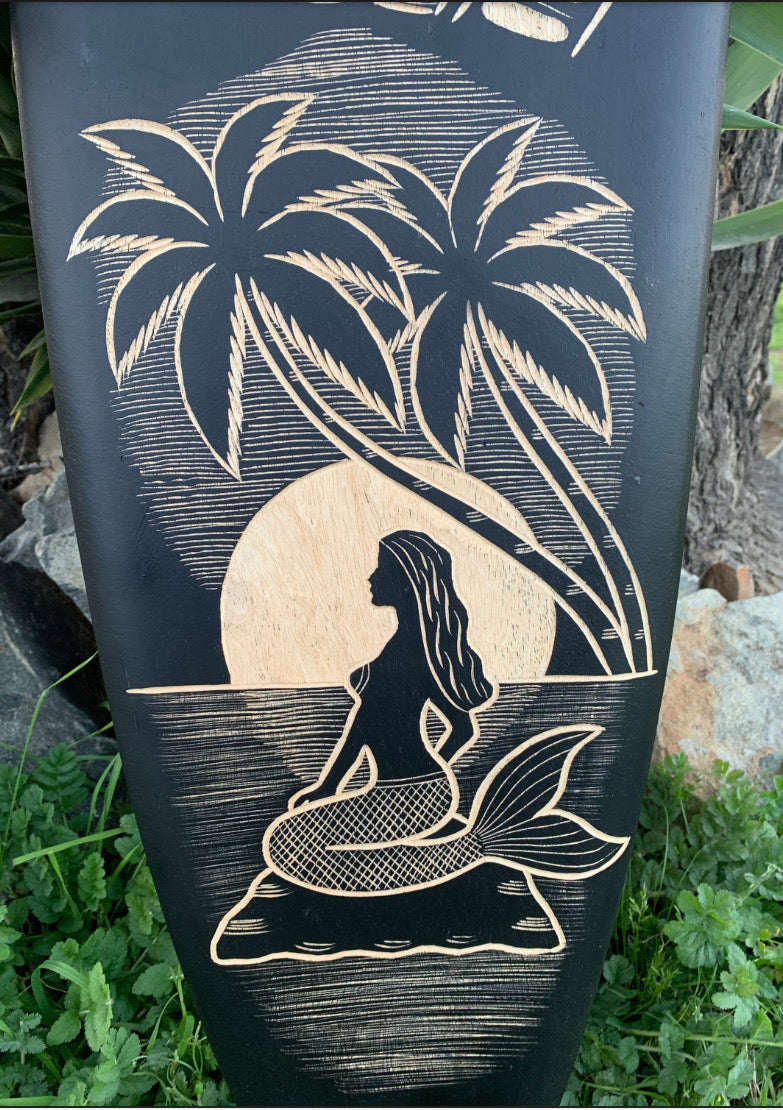 Wooden relief carving of a mermaid with palm trees and a setting sun