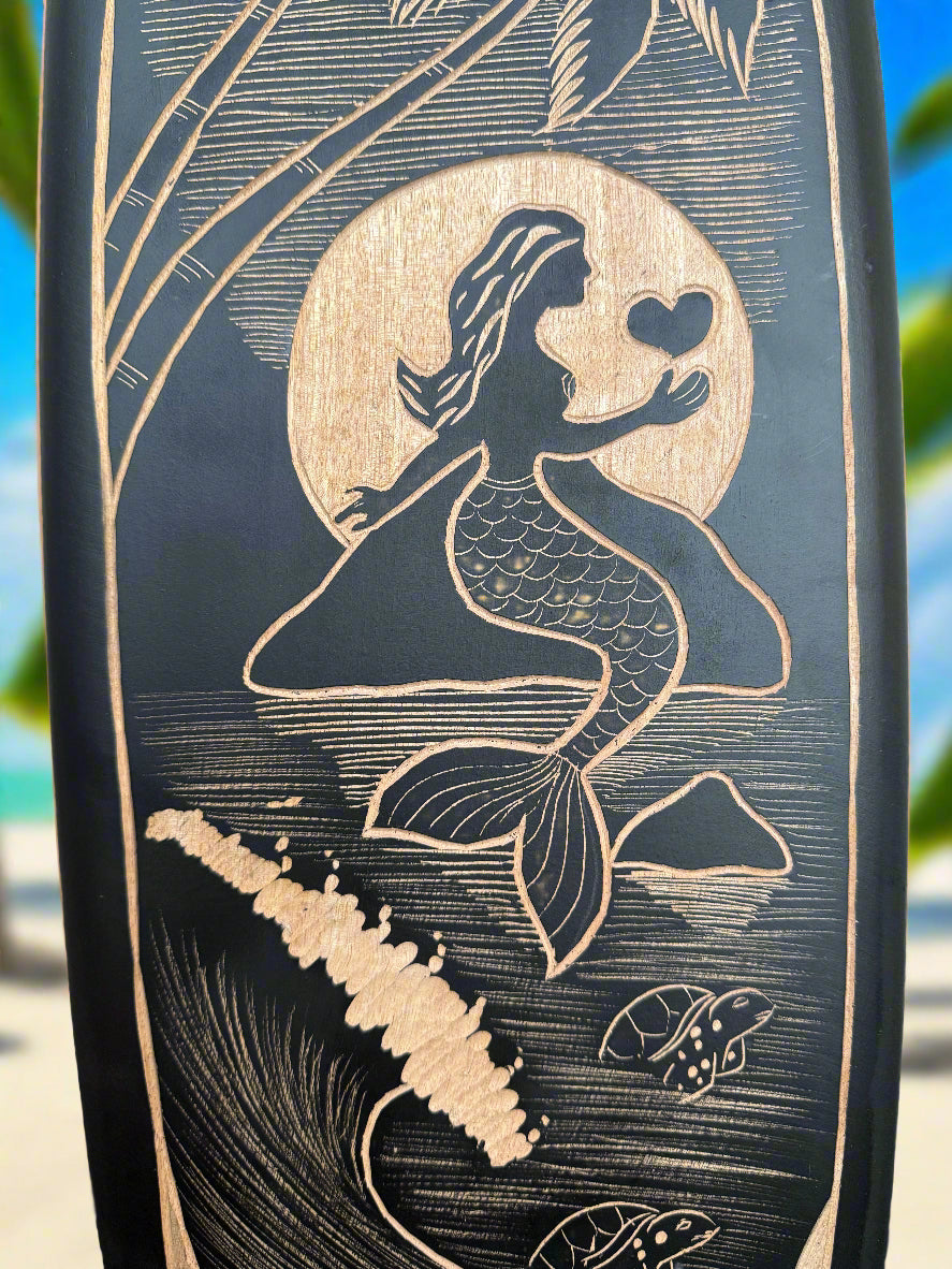 Mermaid silhouette carved on a dark decorative plaque, holding a heart with a sun behind.