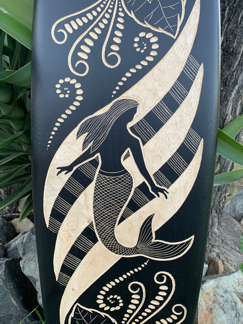 Mermaid silhouette carved in light wood on a dark panel with swirling patterns