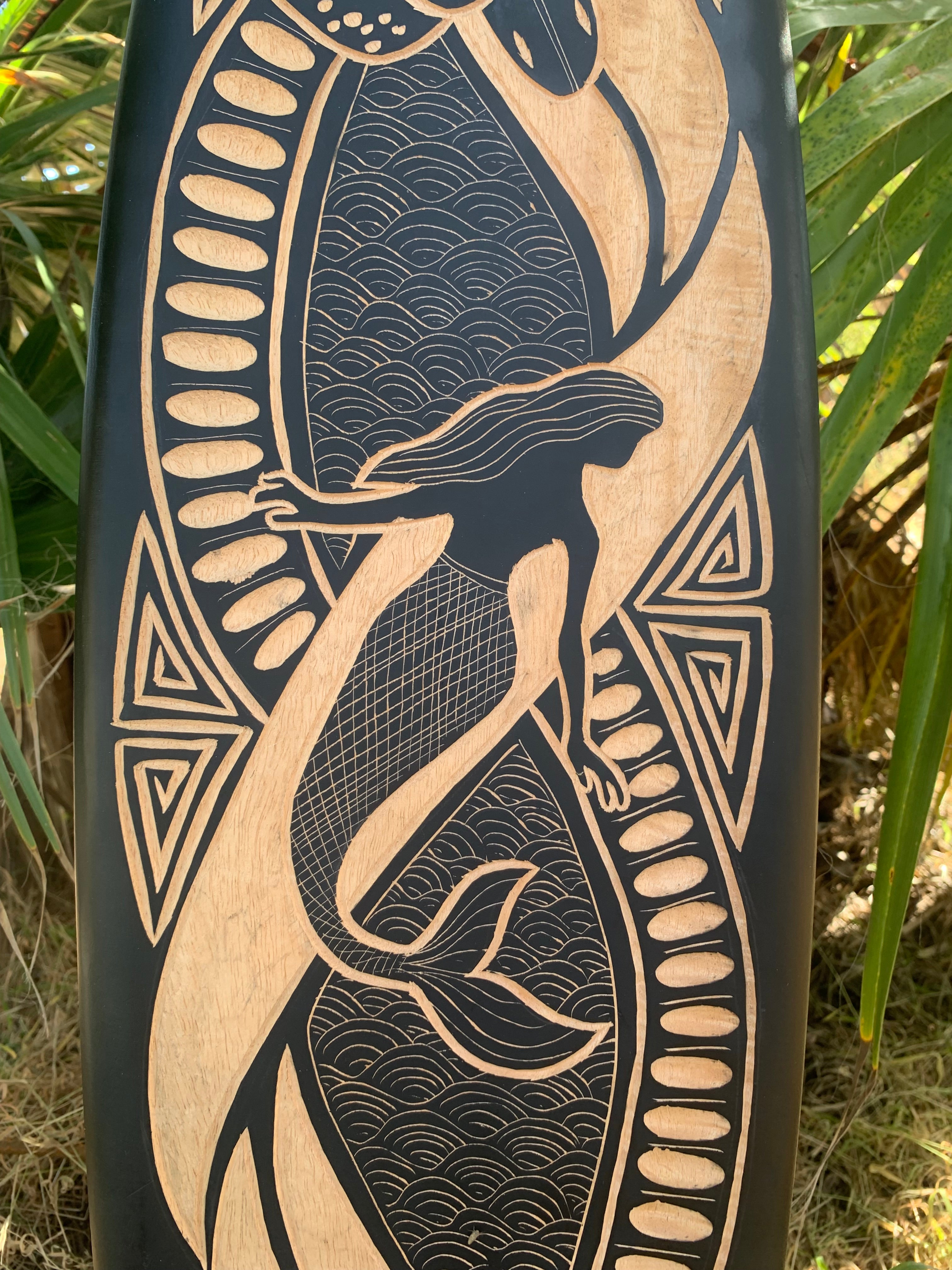 Wooden carving of a mermaid with flowing hair and a fish tail, surrounded by geometric patterns and wave textures